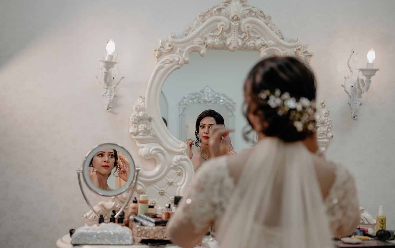 A bride is applying makeup in front of a mirror.