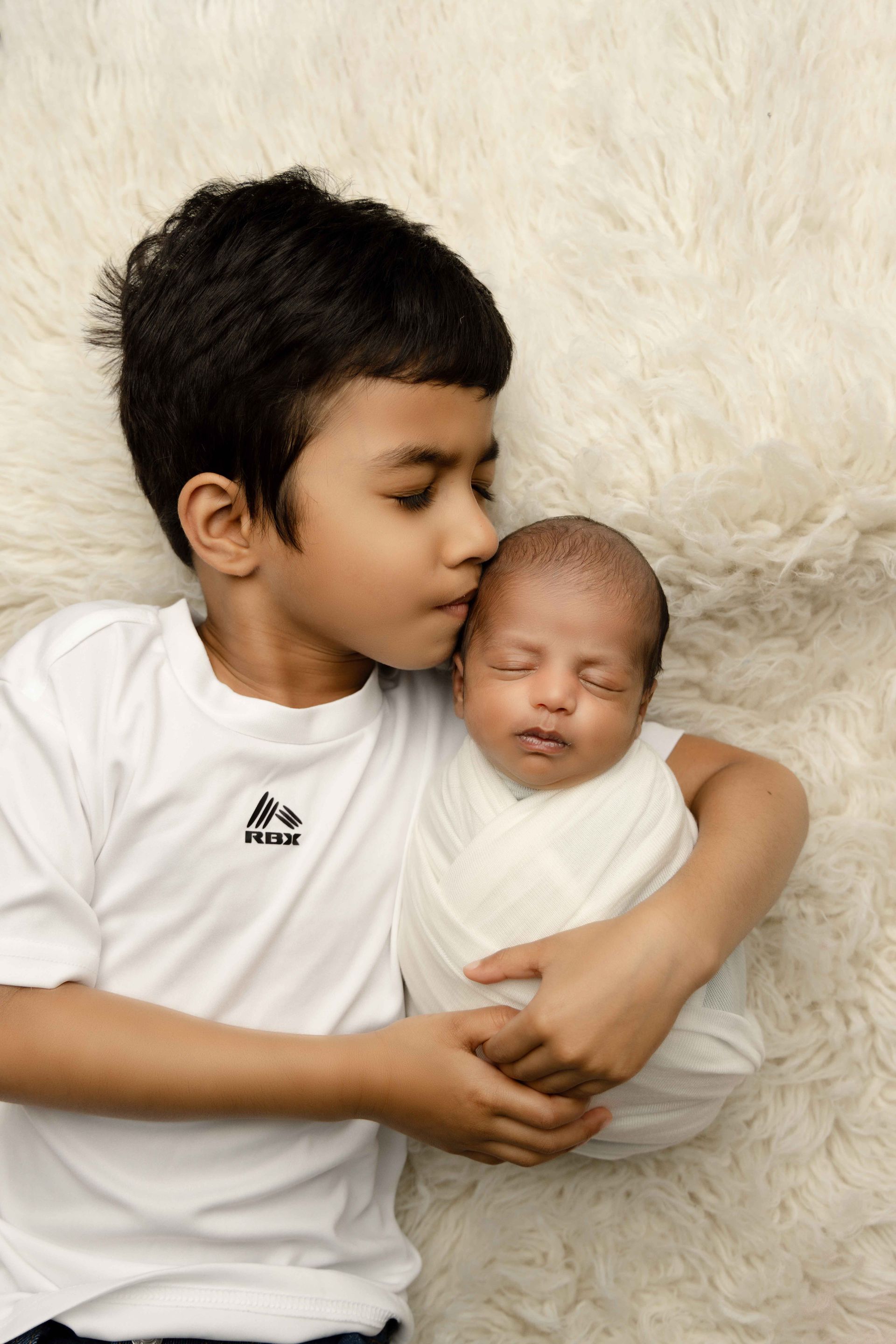 A young boy is holding a newborn baby wrapped in a white blanket.
