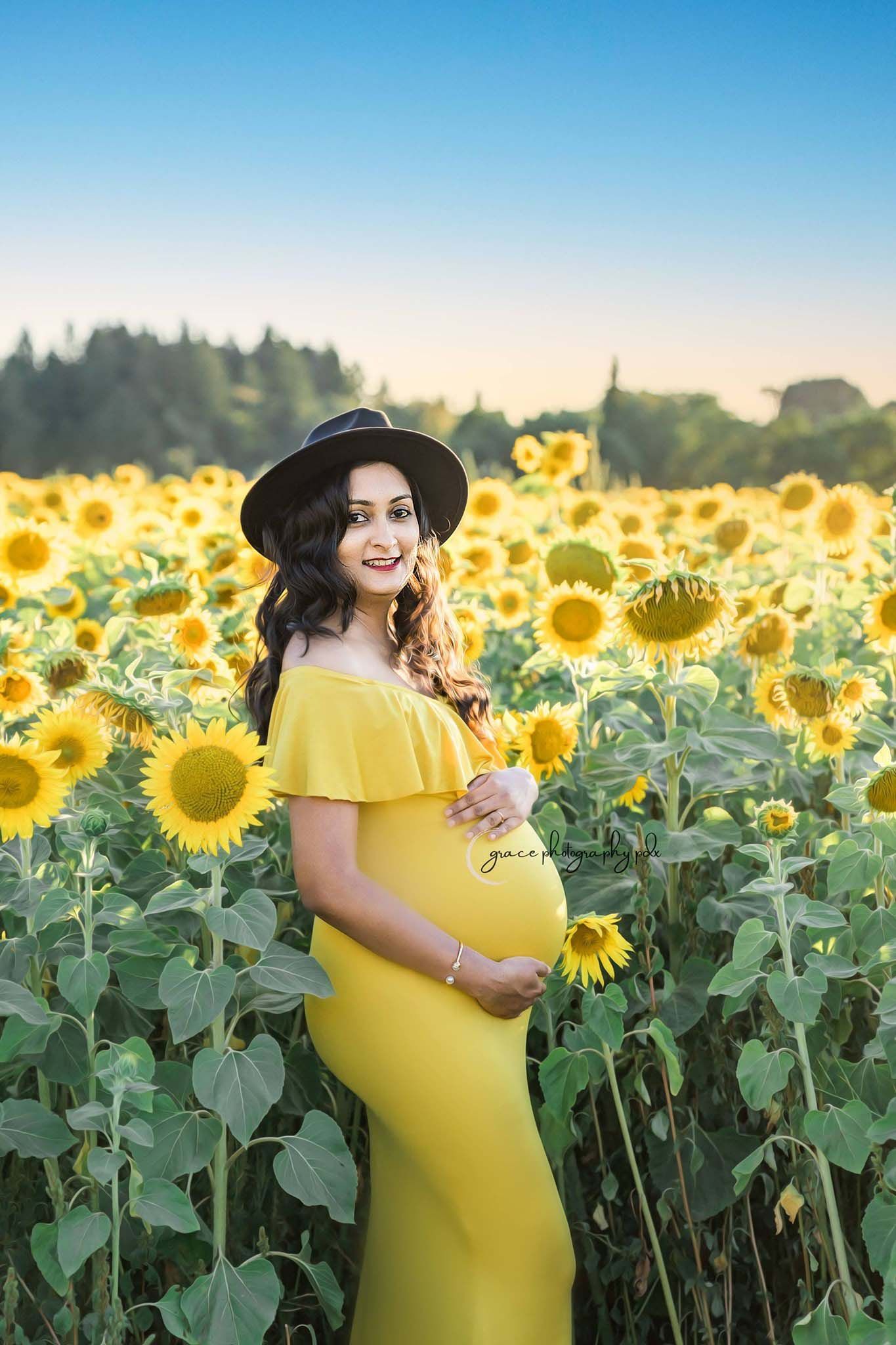 A pregnant woman in a yellow dress is standing in a field of sunflowers.