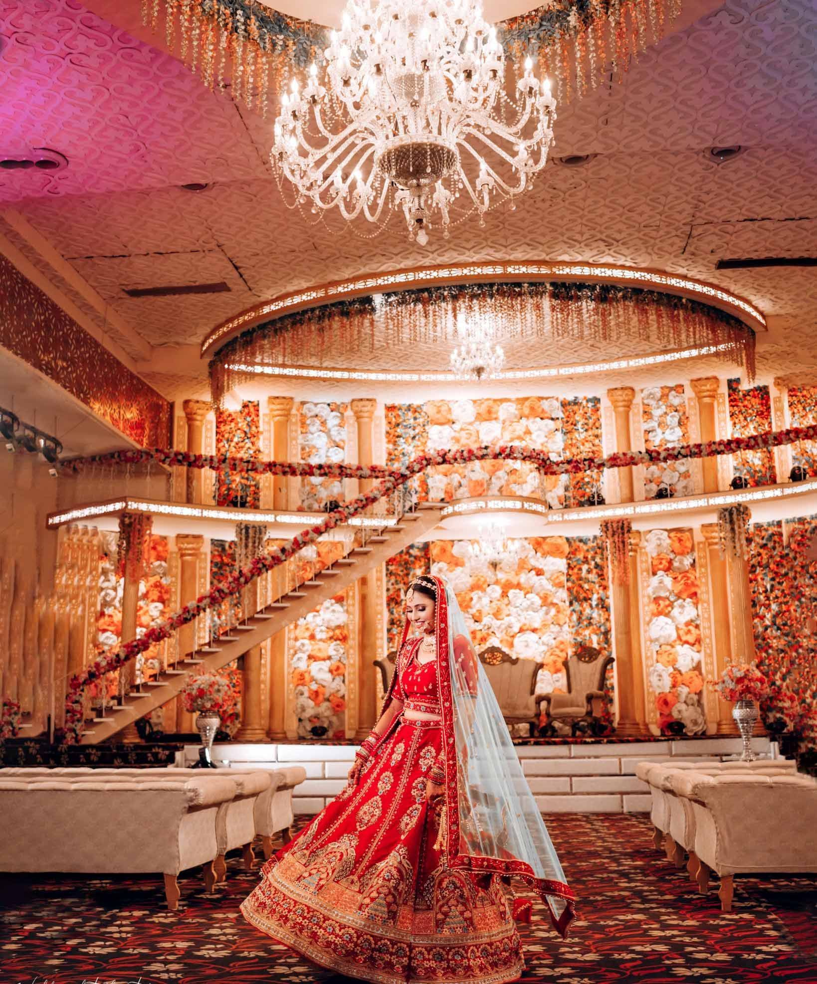 A bride in a red dress is standing in a large room with a chandelier.