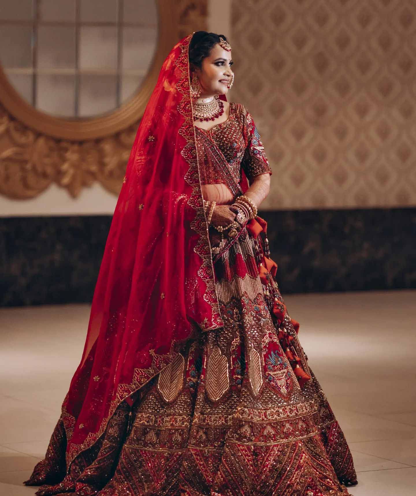 A bride in a red and gold dress is standing in front of a mirror.