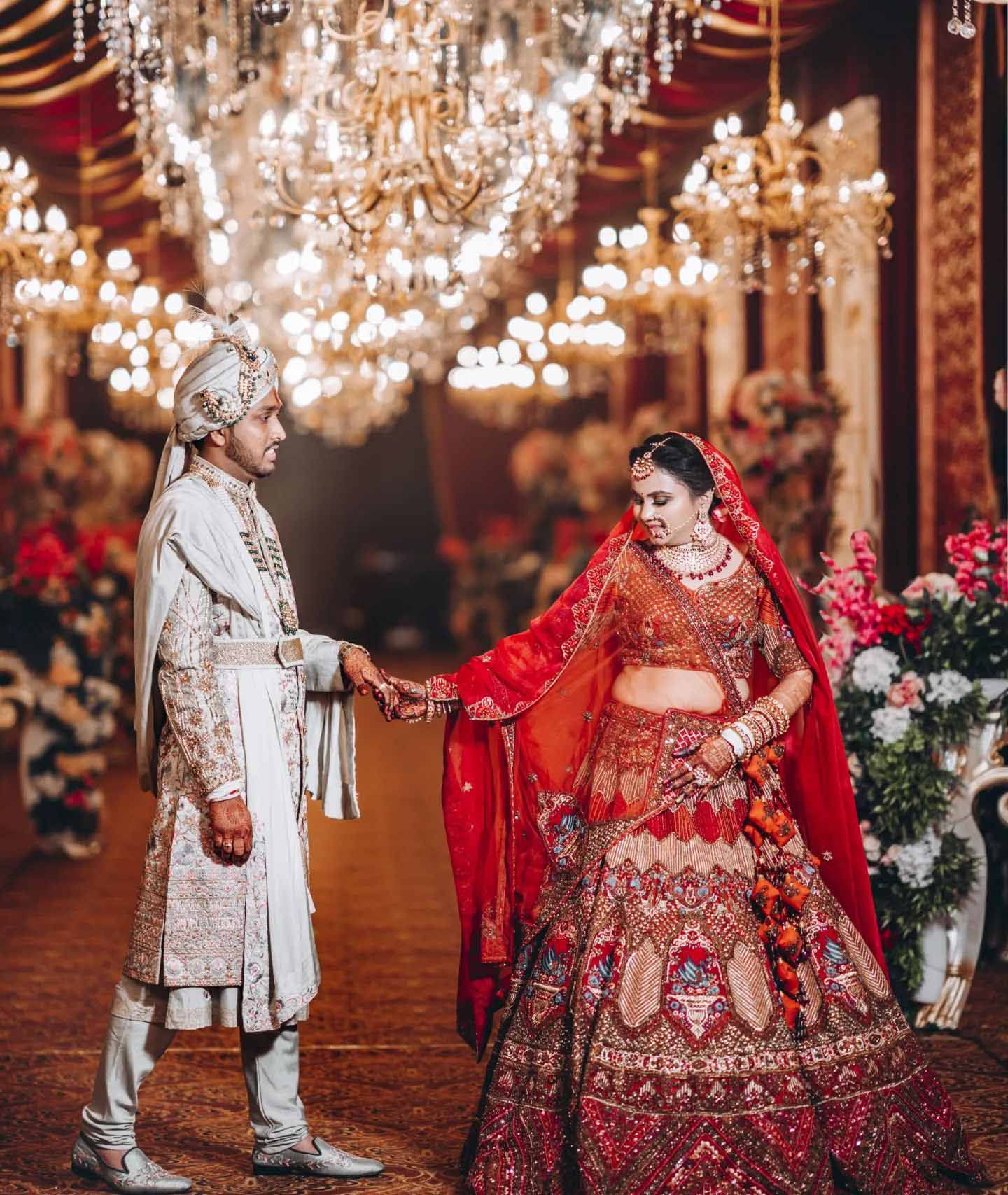 A bride and groom are holding hands in a room with a chandelier.