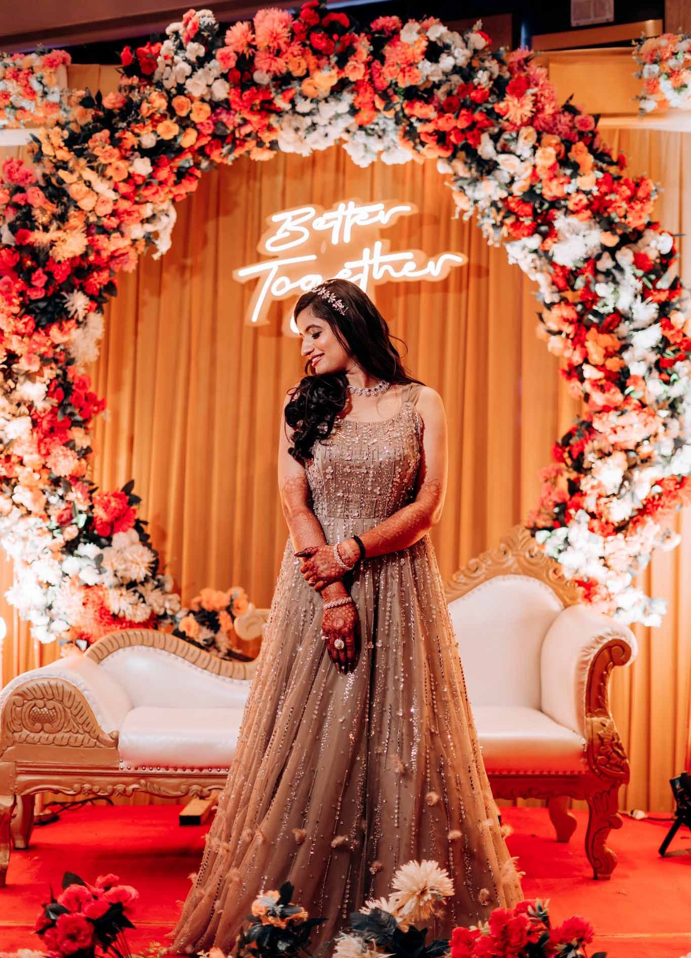 A woman in a long dress is standing in front of a floral arch.