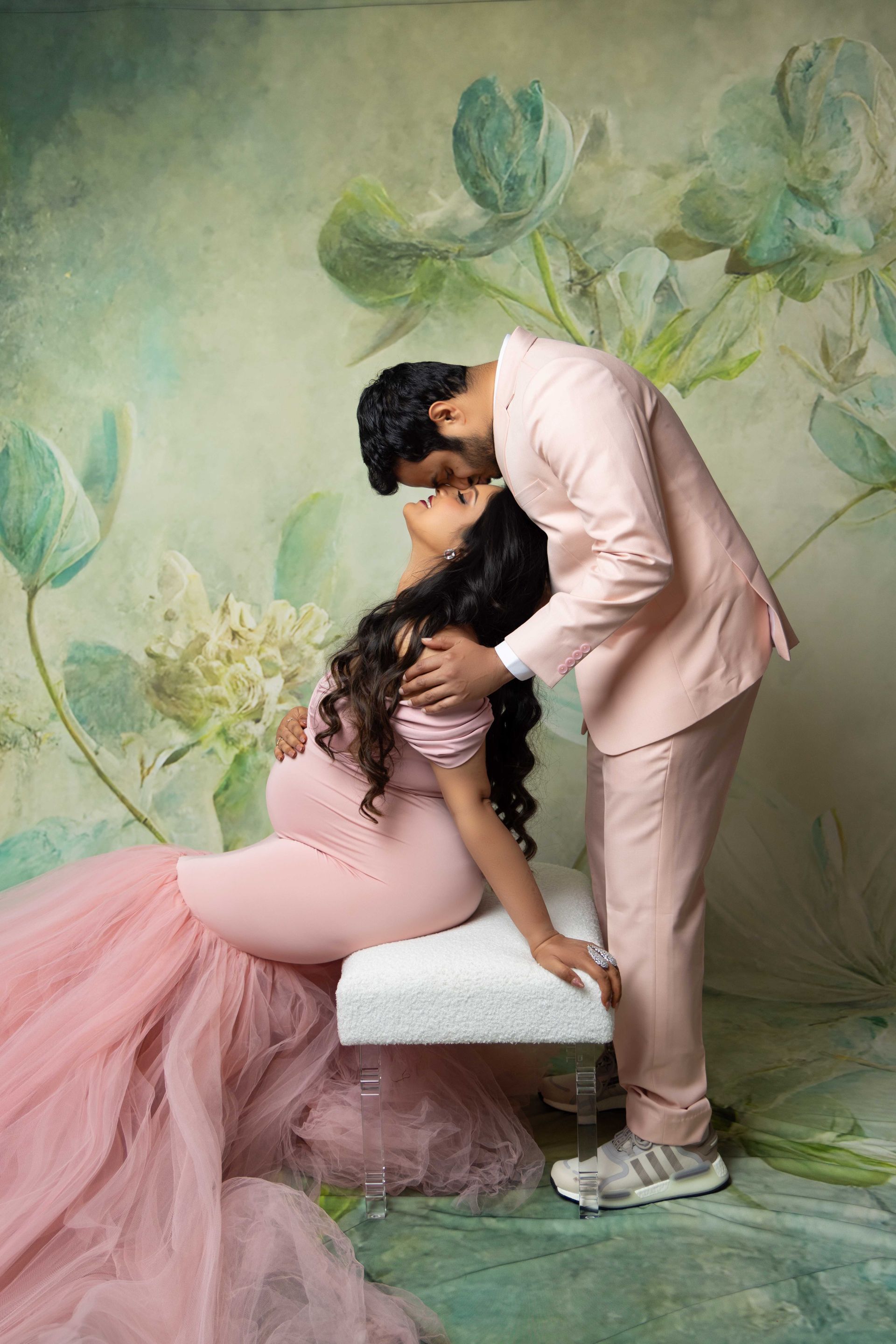 A man in a pink suit is kissing a pregnant woman in a pink dress.