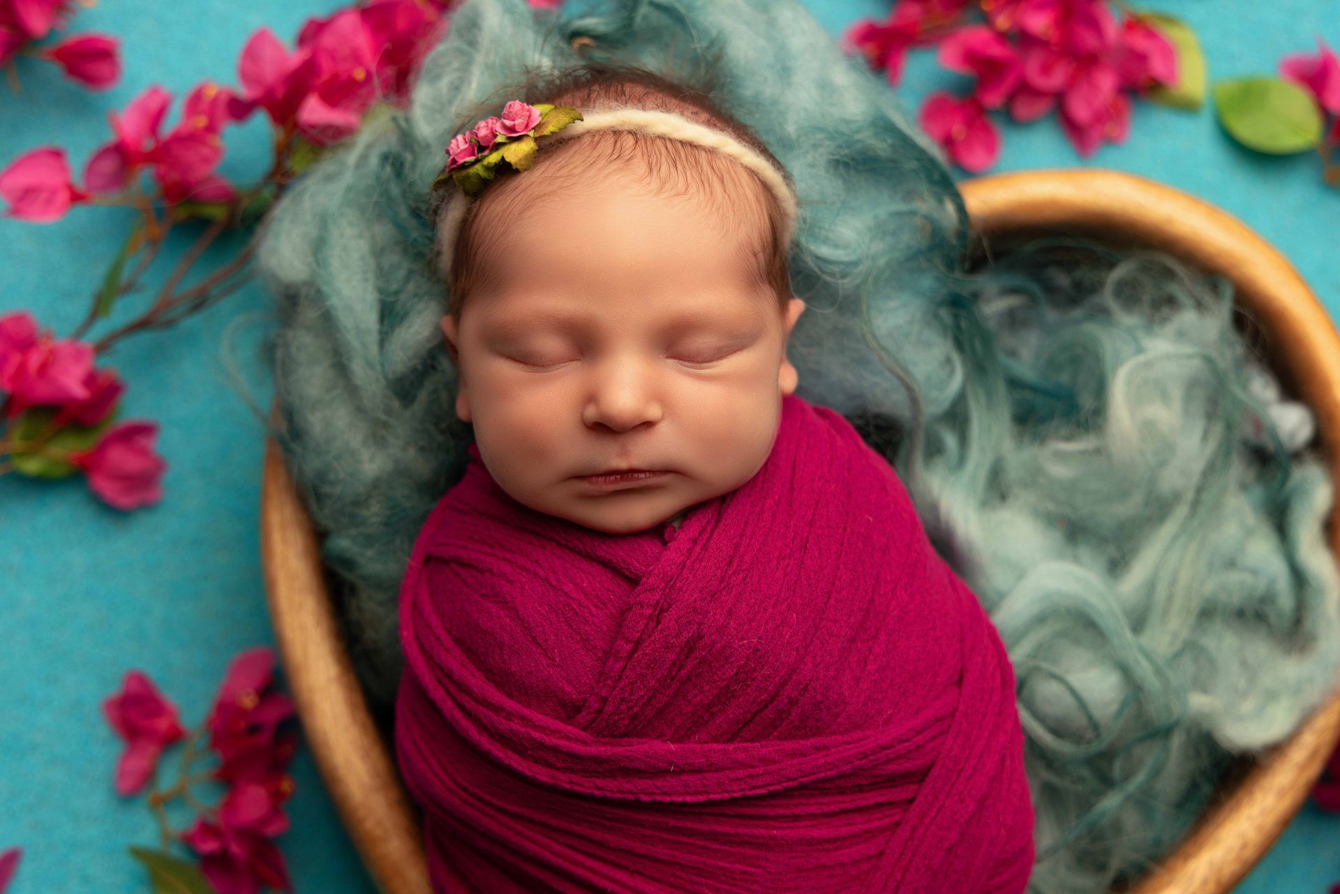 A newborn baby wrapped in a pink blanket is sleeping in a heart shaped basket.