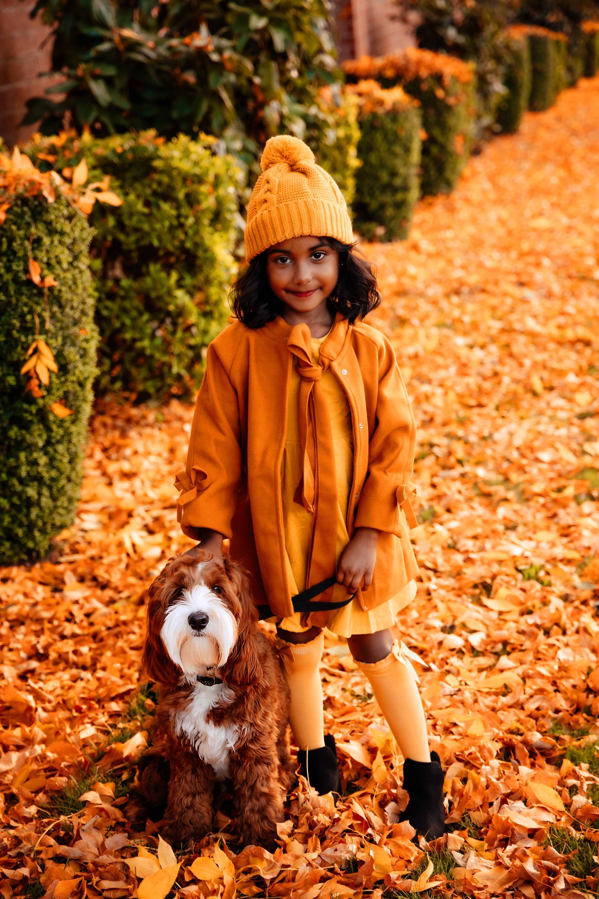 A little girl is standing next to a stuffed dog in a pile of leaves.
