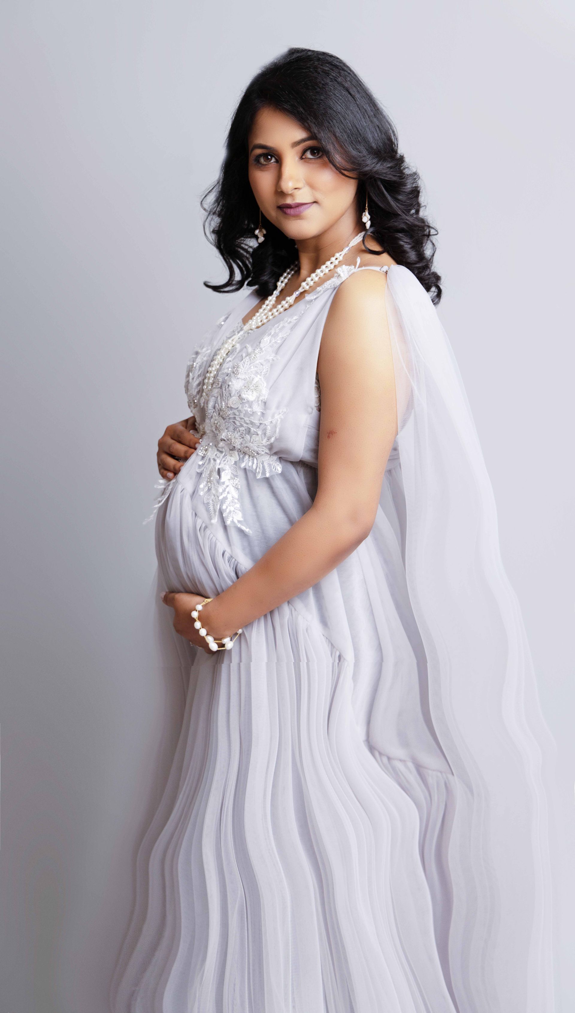 A pregnant woman in a white dress is holding her belly.