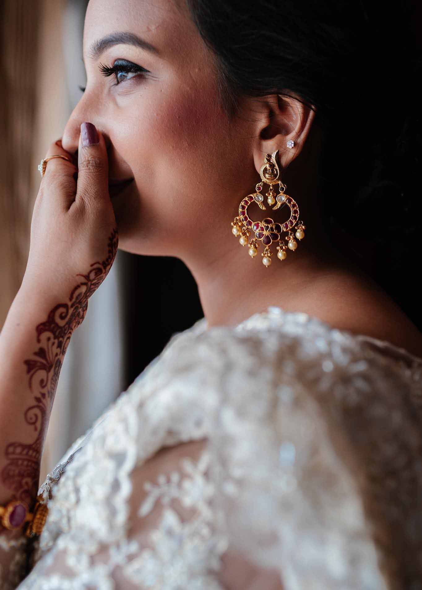 A woman wearing a white dress and earrings is covering her mouth with her hand.