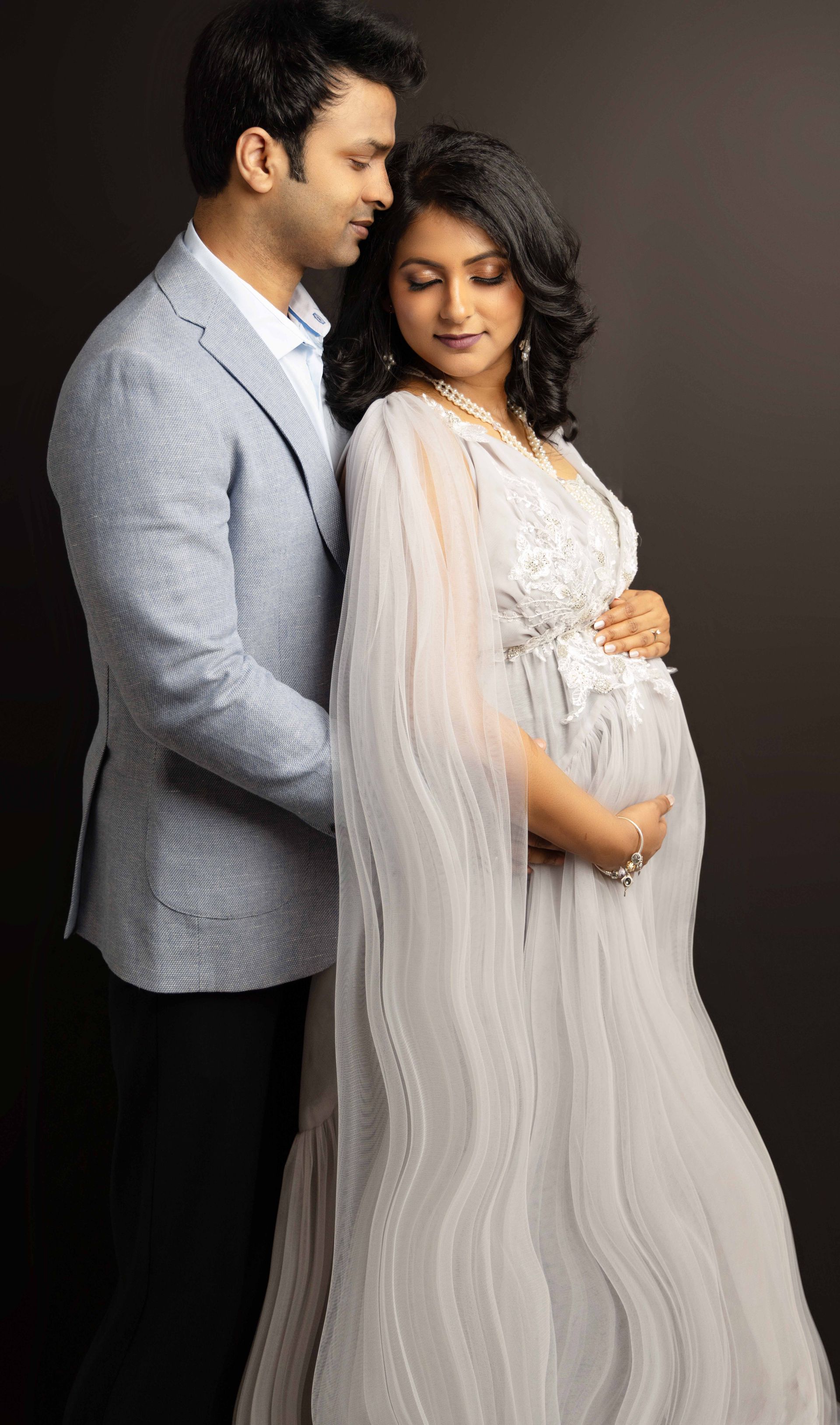 A man is standing next to a pregnant woman in a white dress.