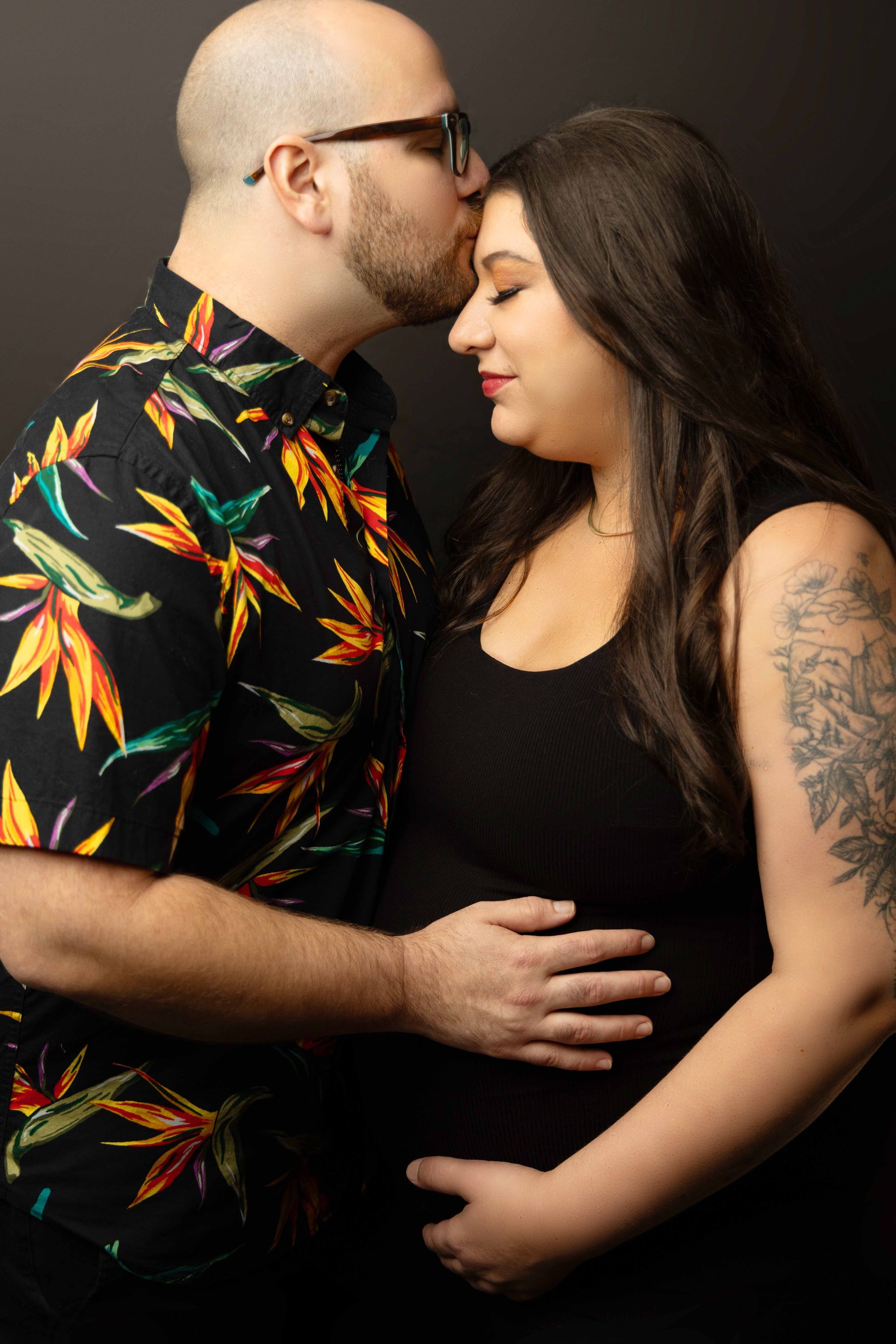 A man is kissing a pregnant woman on the forehead.