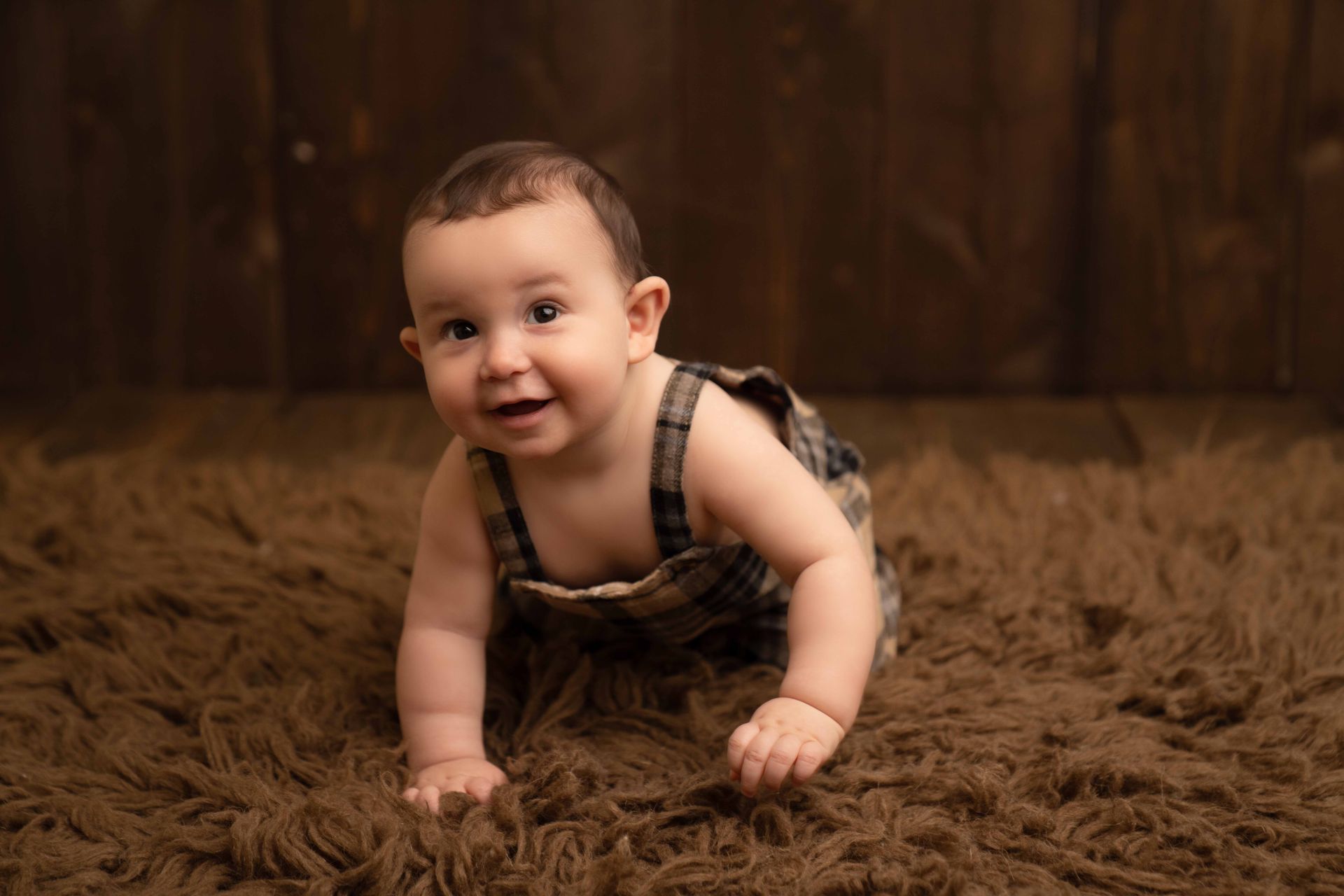 A baby is crawling on a brown carpet and smiling.