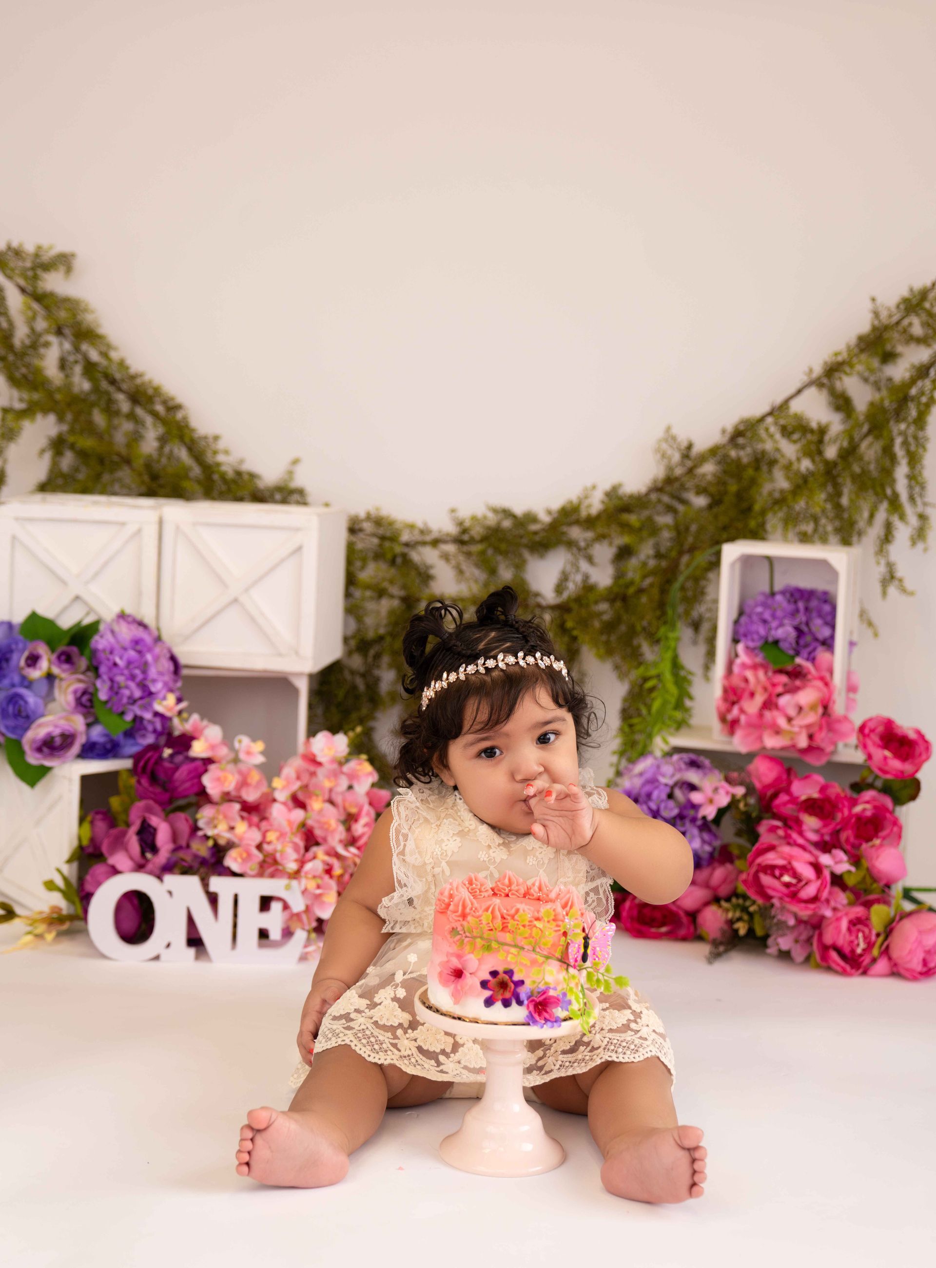 A baby girl is sitting on the floor eating a cake.