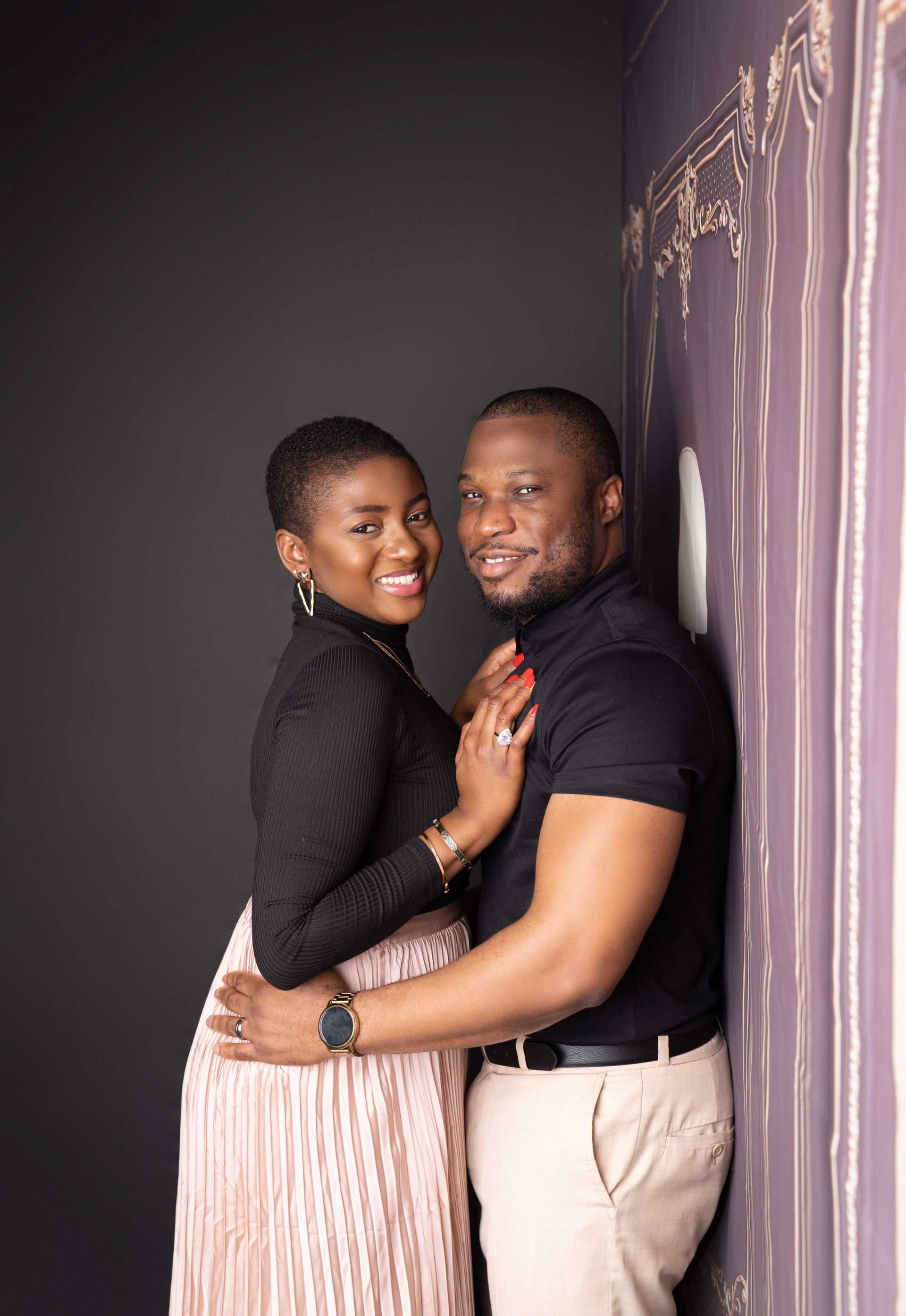 A man and a woman are posing for a picture while leaning against a wall.