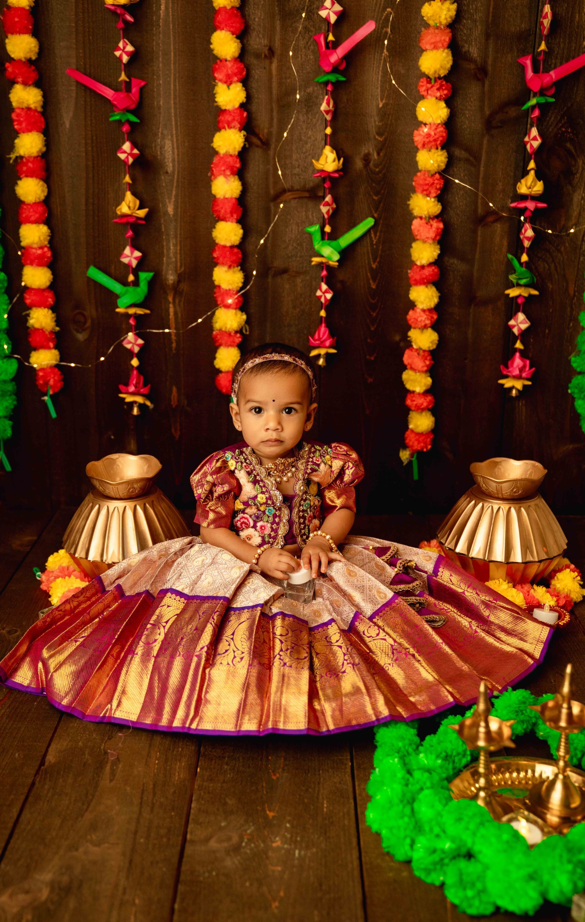 A little girl in a dress is sitting on a wooden floor.