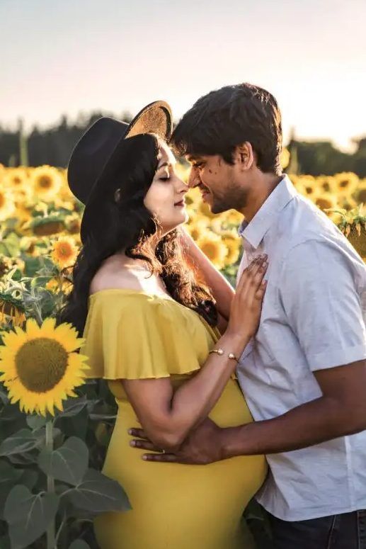 A man and a pregnant woman are kissing in a field of sunflowers