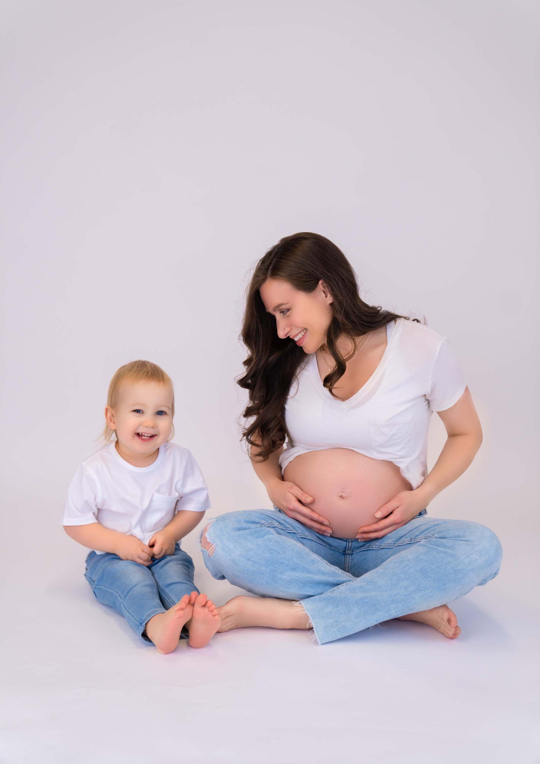A pregnant woman is sitting on the floor next to a little child