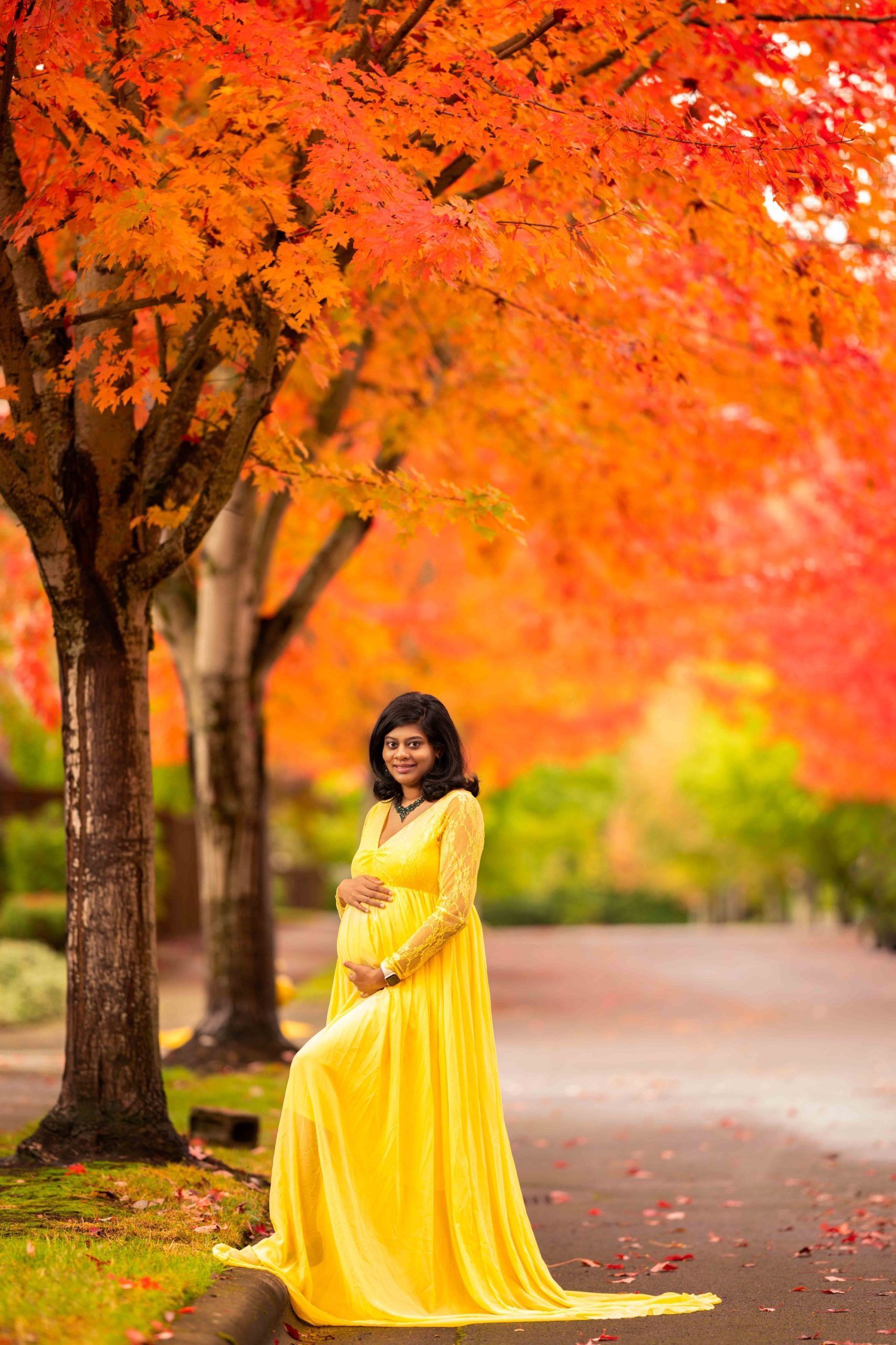 A pregnant woman in a yellow dress is standing in front of a tree