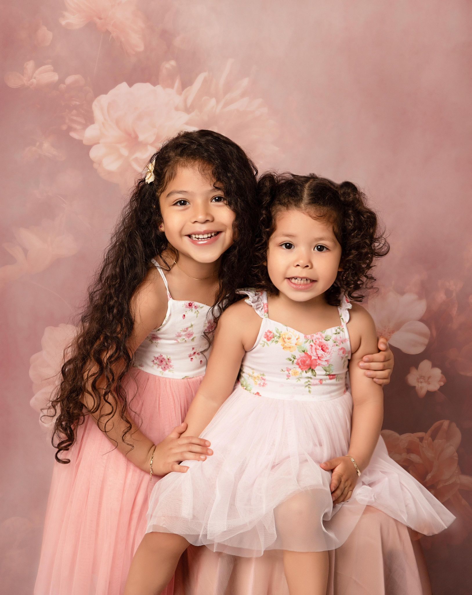 Two little girls are posing for a picture together in front of a pink background.