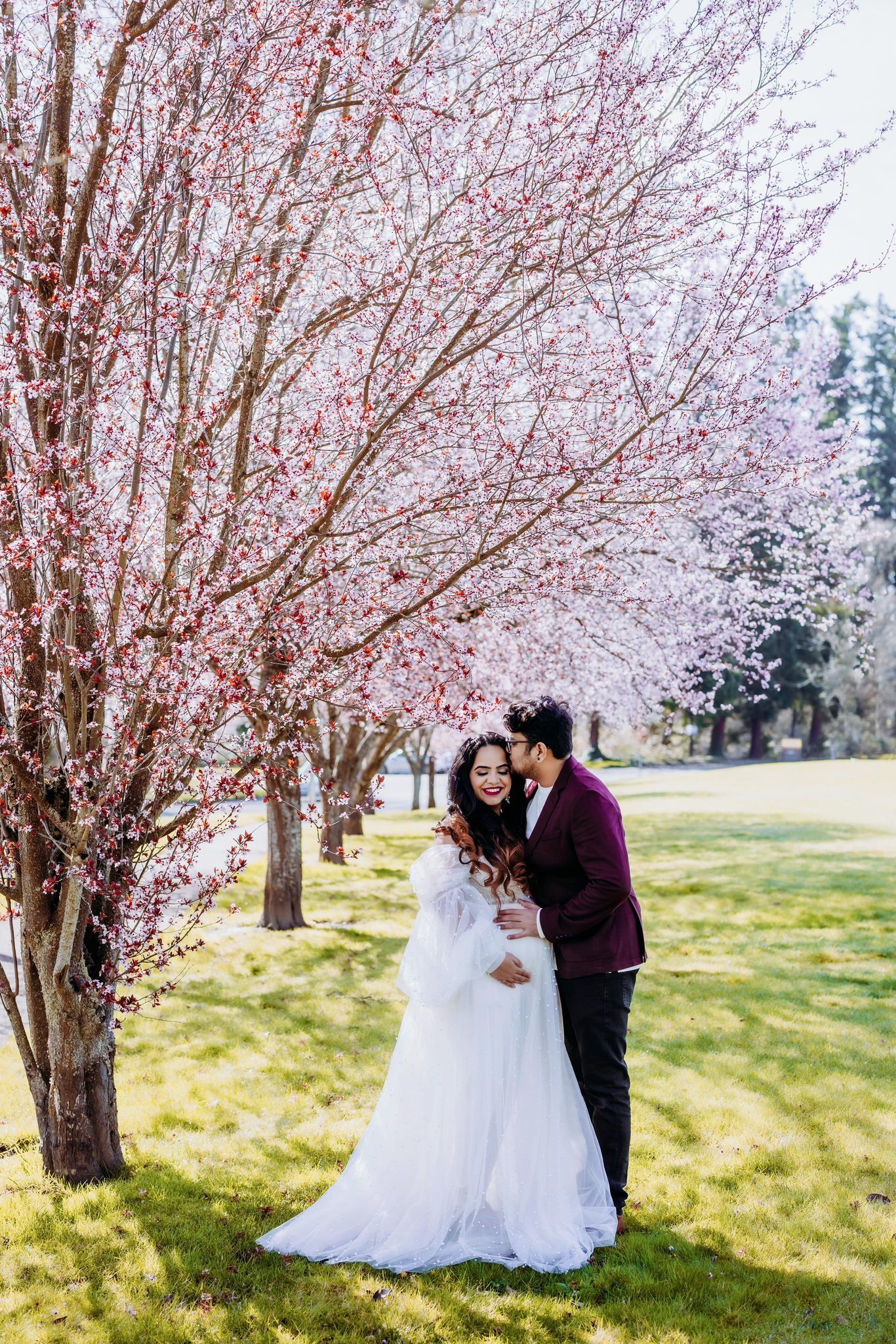 A bride and groom are posing for a picture under a cherry blossom tree.