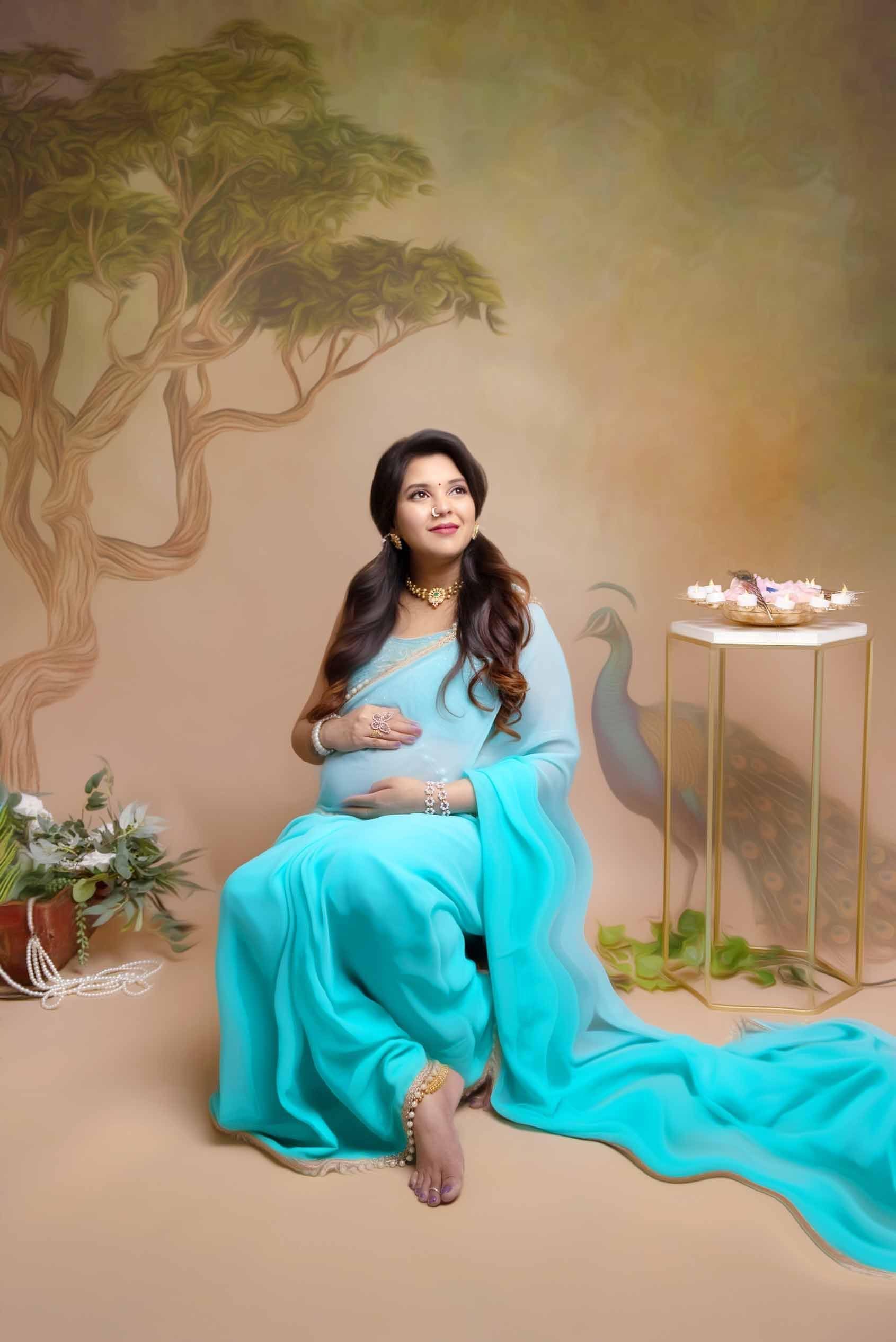A pregnant woman in a blue saree is sitting on the floor.