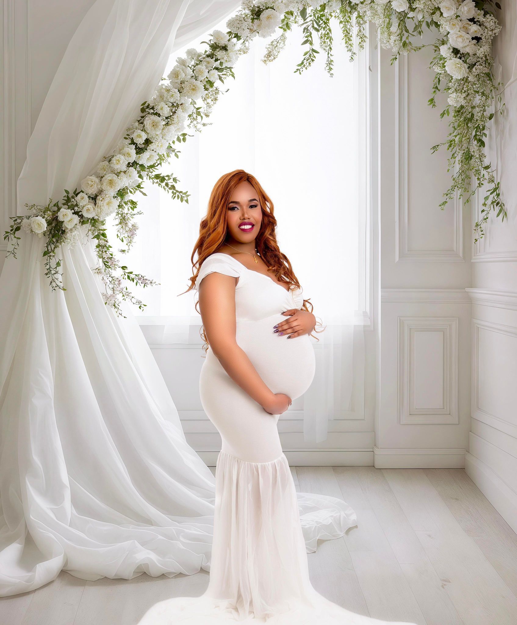 A pregnant woman in a white dress is standing in front of a window.