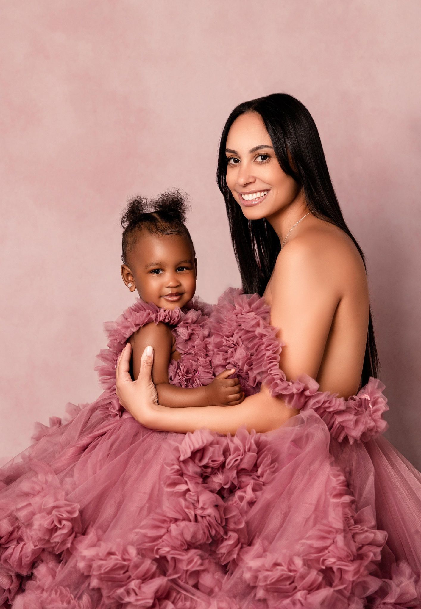 A woman in a pink dress is holding a baby in her arms.