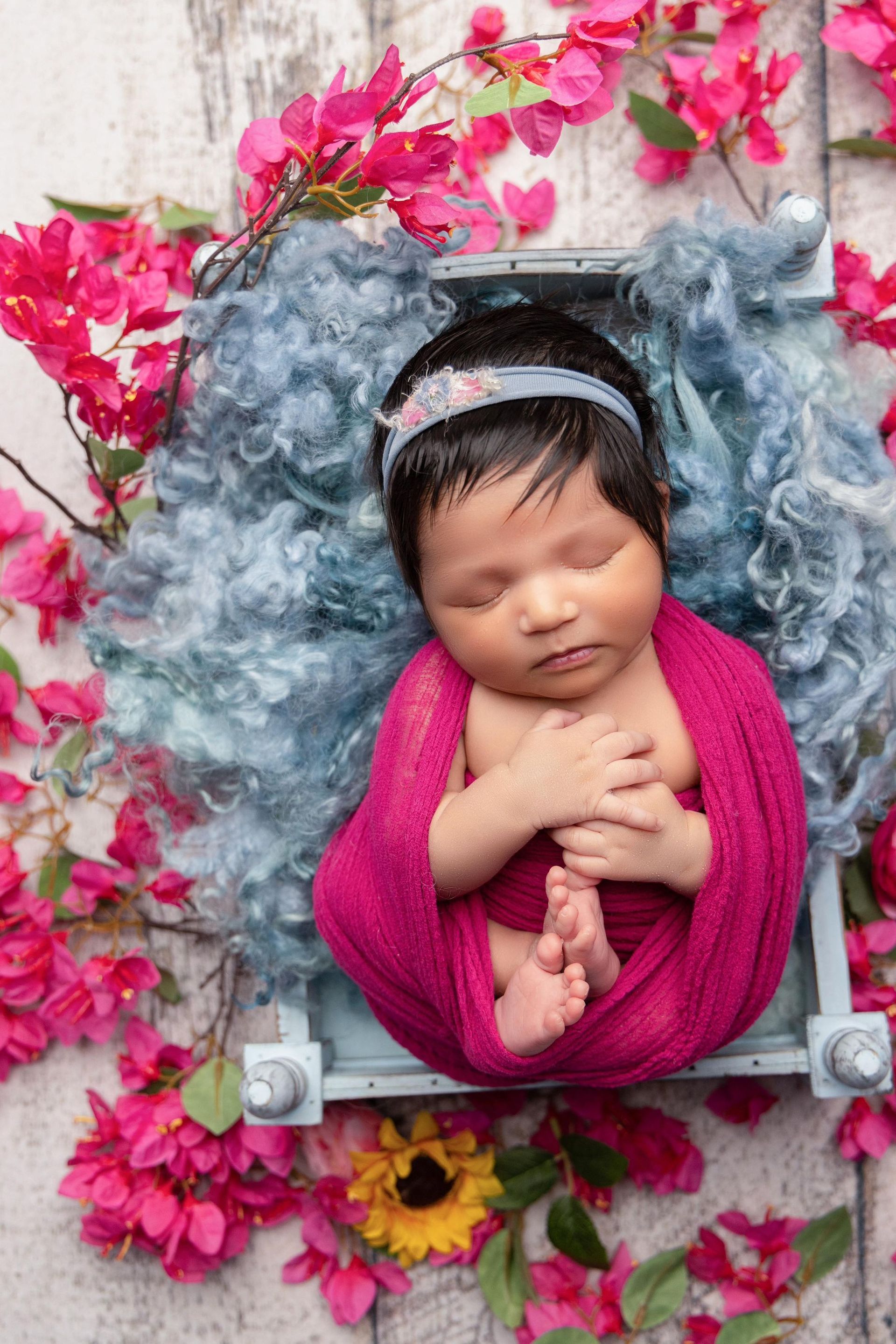 A newborn baby is sleeping in a crate surrounded by pink flowers.