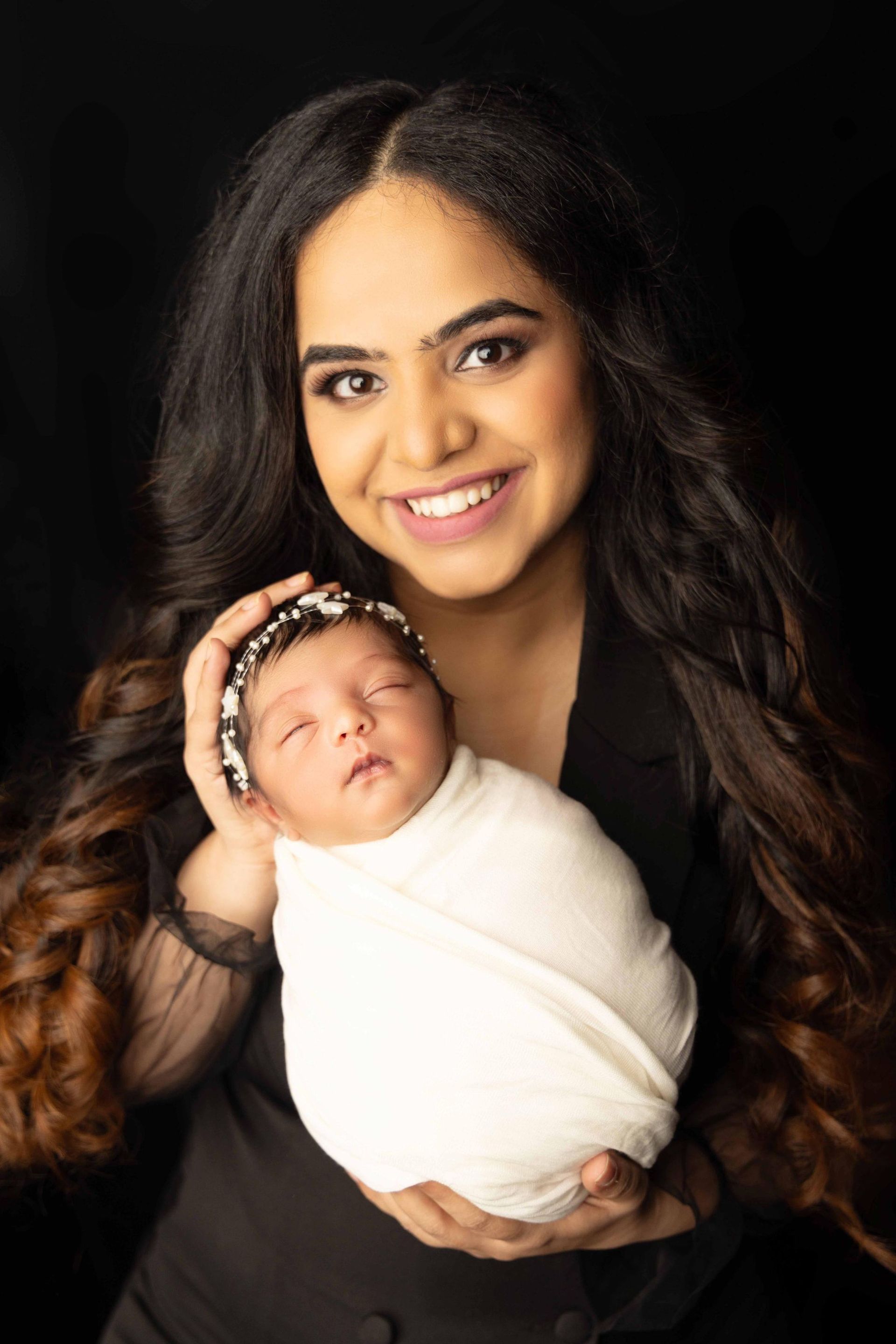 A woman is holding a newborn baby wrapped in a white blanket.