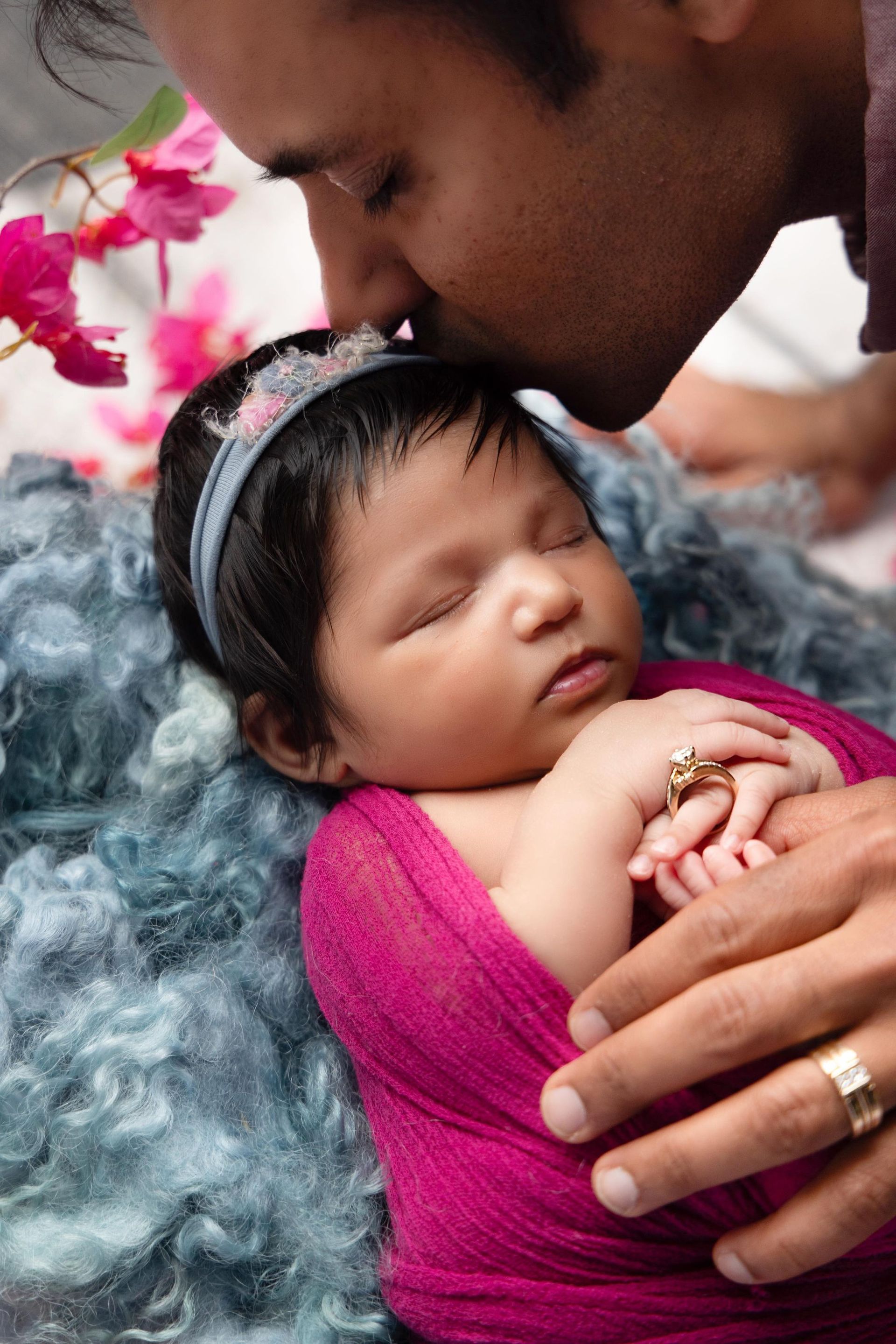 A newborn baby is sleeping while its parent kisses its forehead
