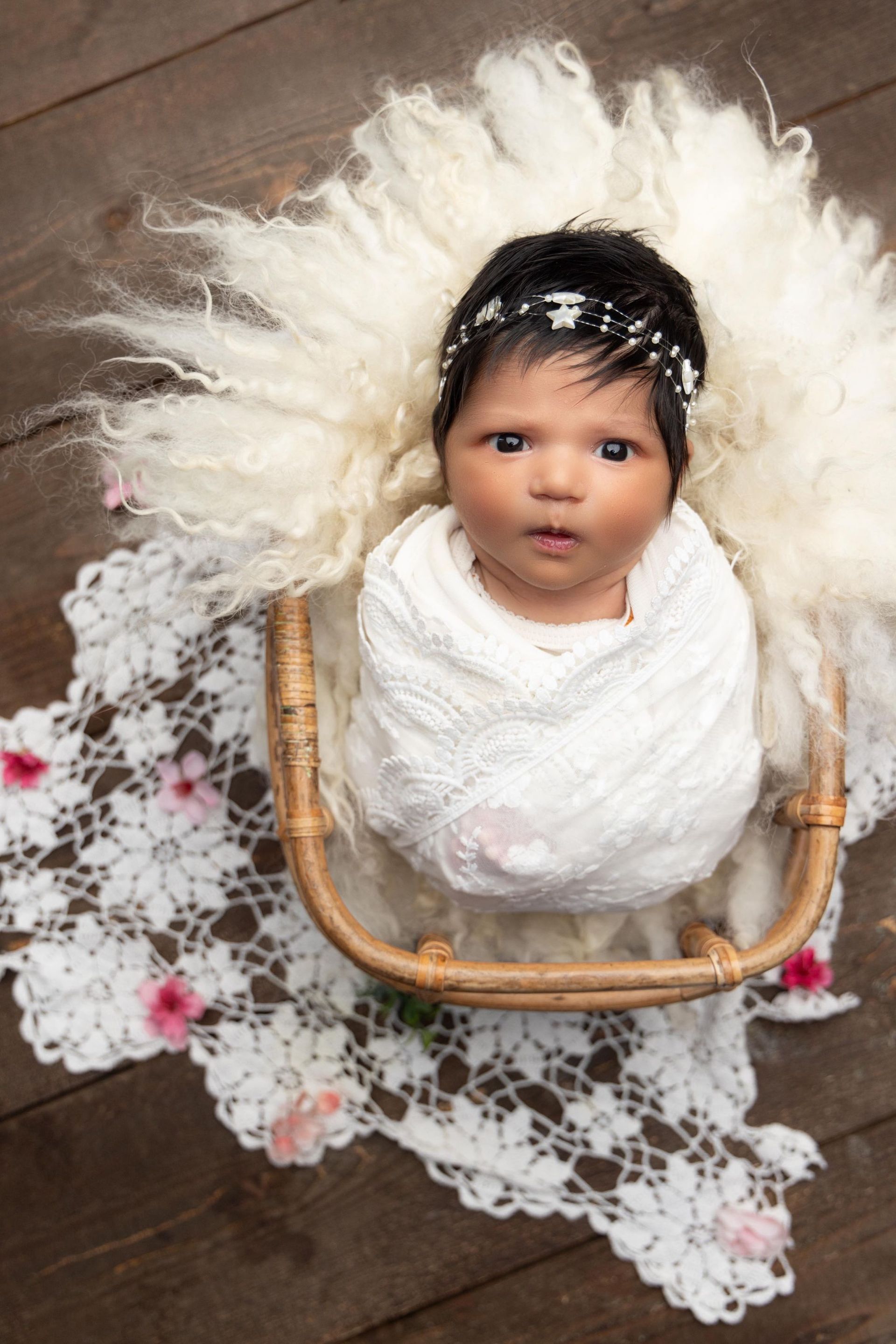 A newborn baby is wrapped in a white blanket in a wicker basket.