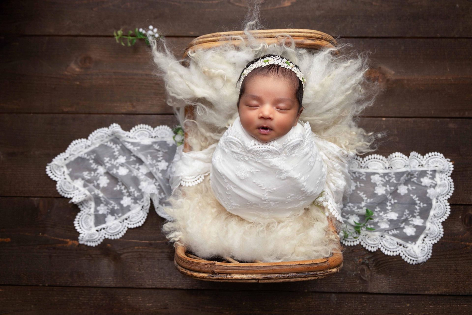 A newborn baby wrapped in a white blanket is laying in a wicker basket.