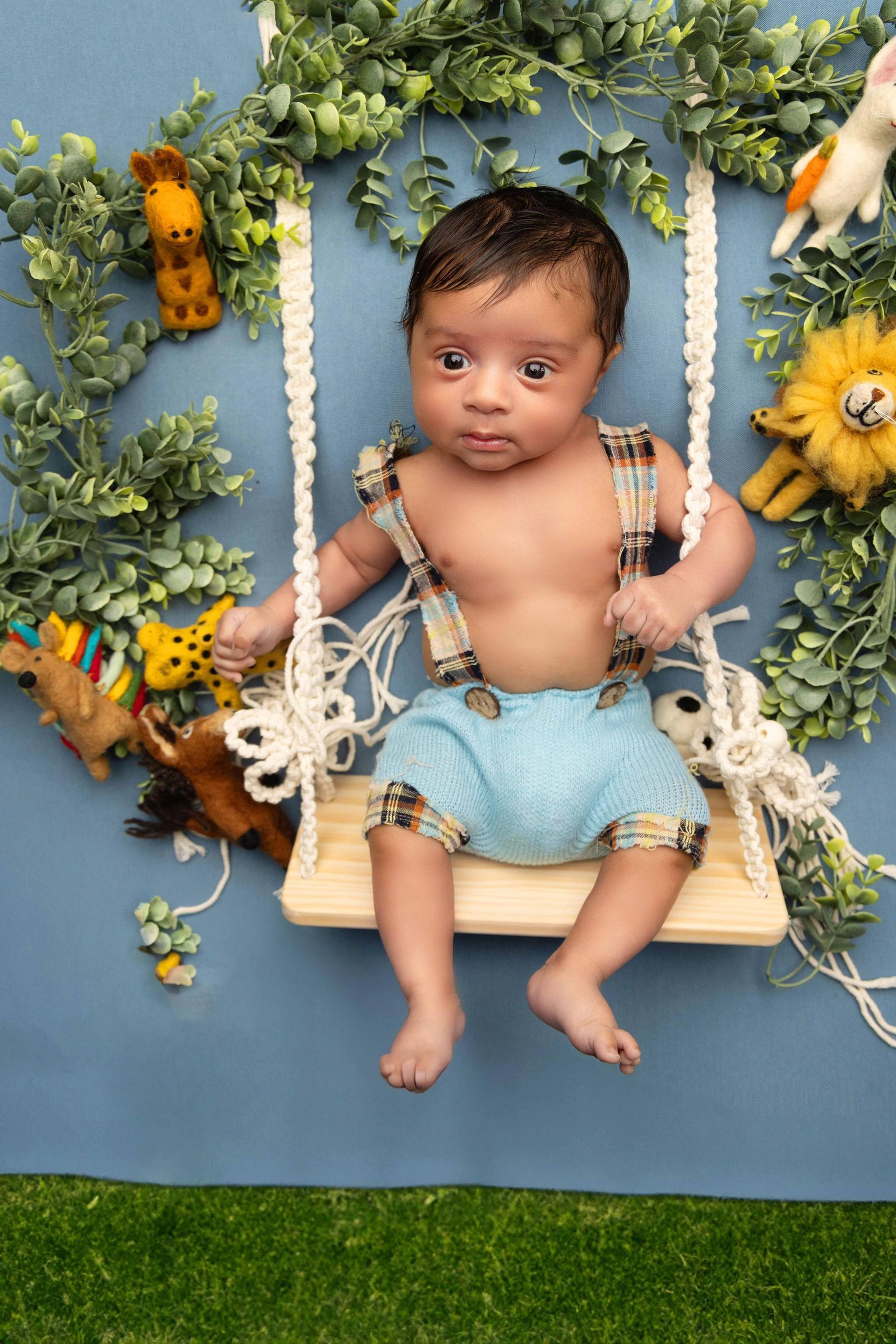 A baby is sitting on a wooden swing surrounded by stuffed animals.