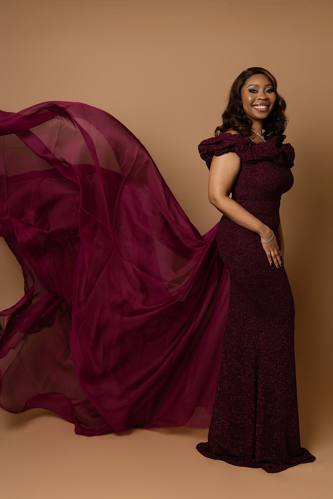 A woman in a long purple dress is standing in front of a brown background.