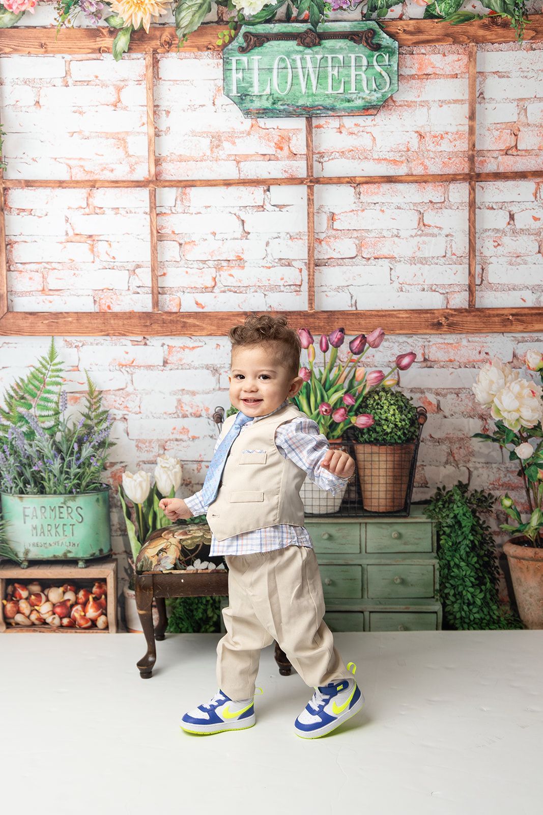 A little boy is standing in front of a brick wall with potted plants.