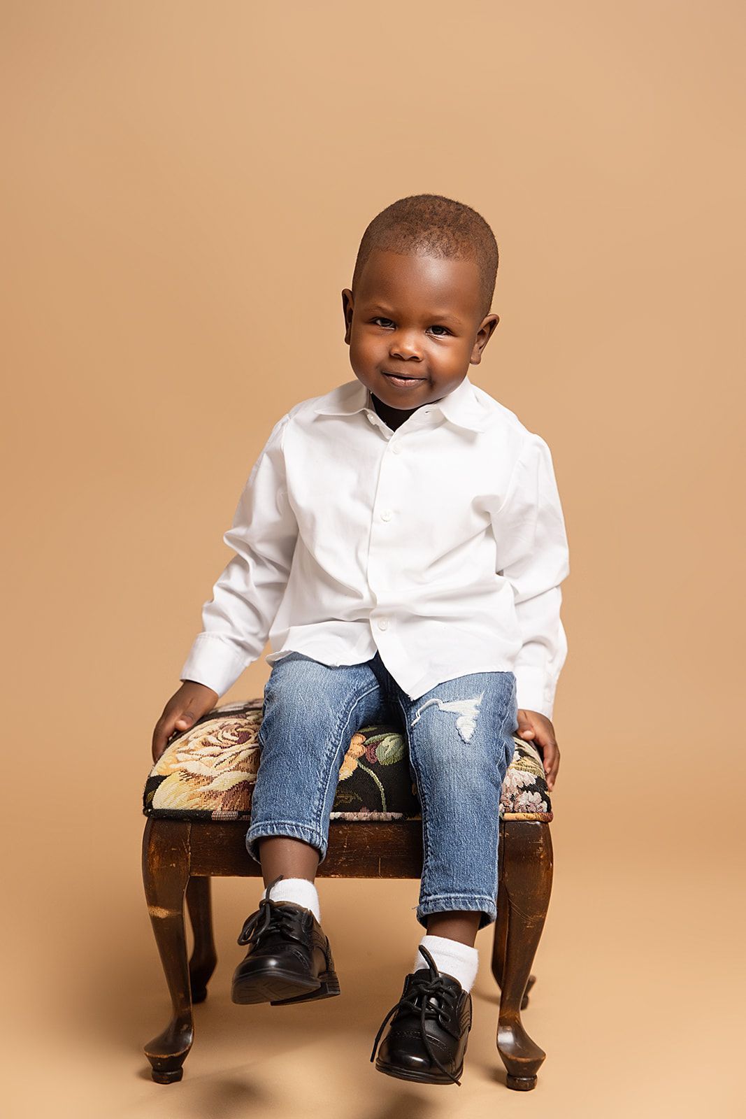 A little boy is sitting on a chair wearing a white shirt and jeans.