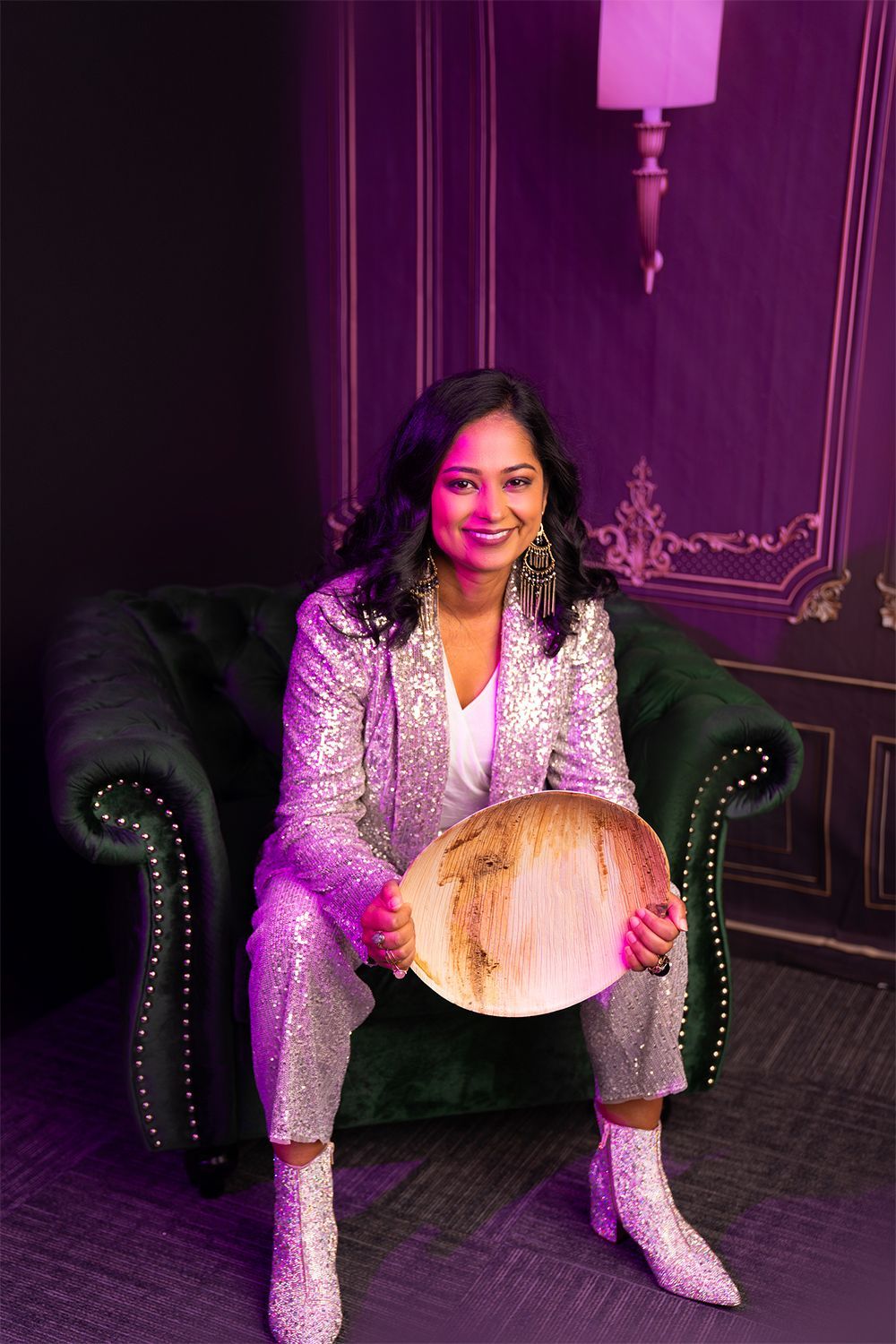 A woman in a sequined suit is sitting in a chair holding a plate