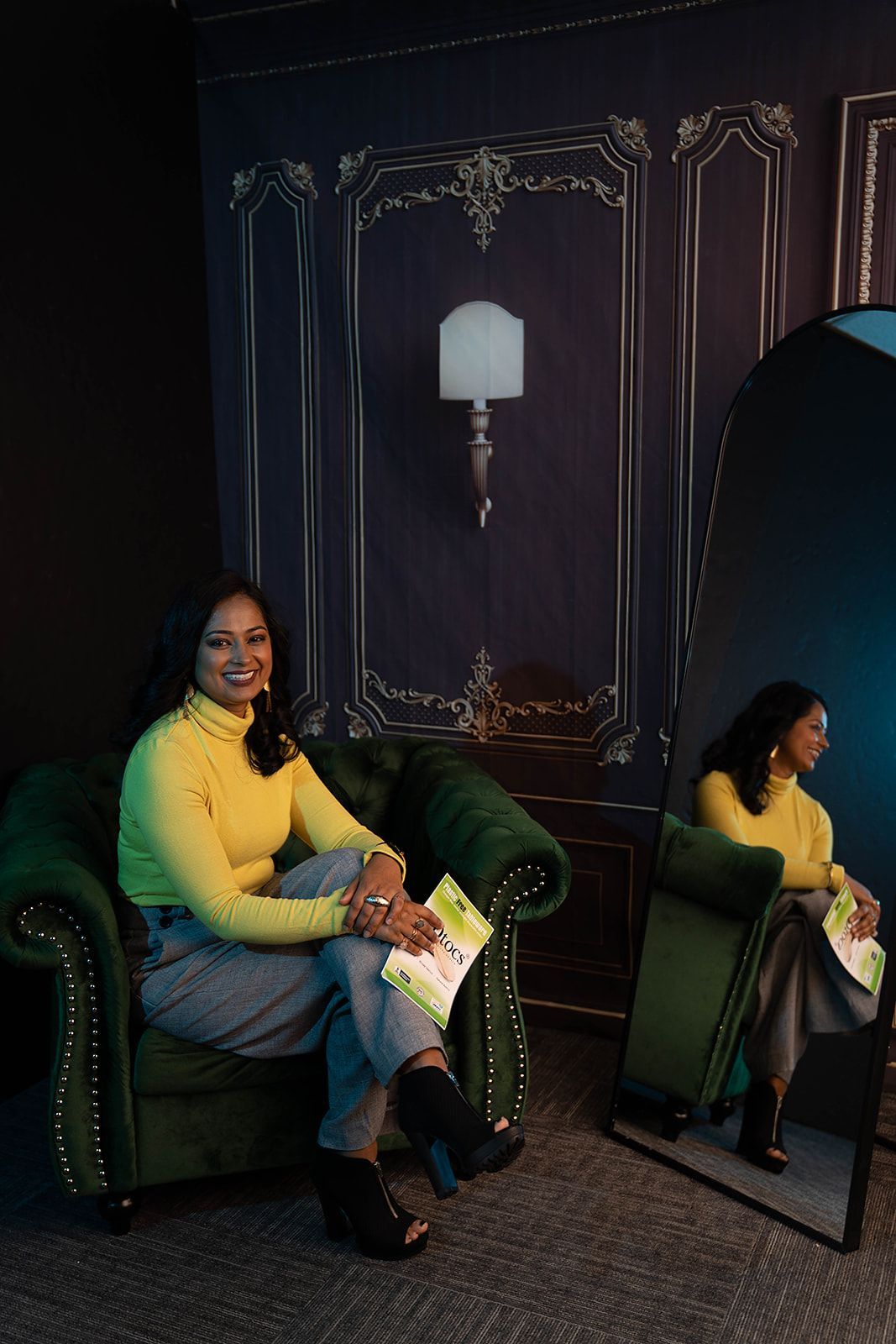 A woman is sitting in a green chair in front of a mirror