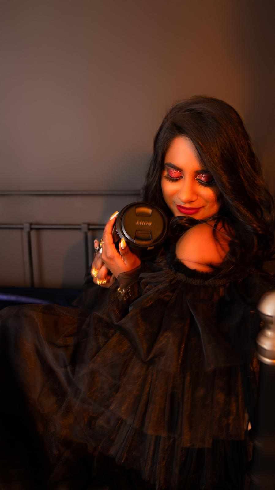 A woman in a black dress is sitting on a couch holding a camera