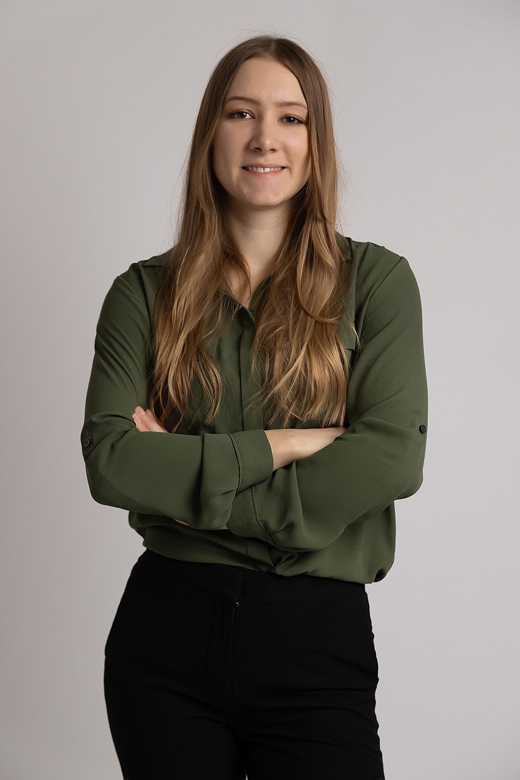 A woman in a green shirt and black pants is standing with her arms crossed