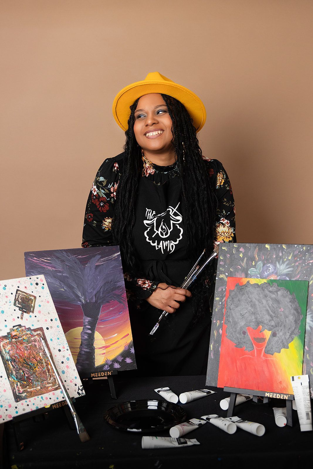 A woman in a yellow hat is standing in front of a table with paintings.