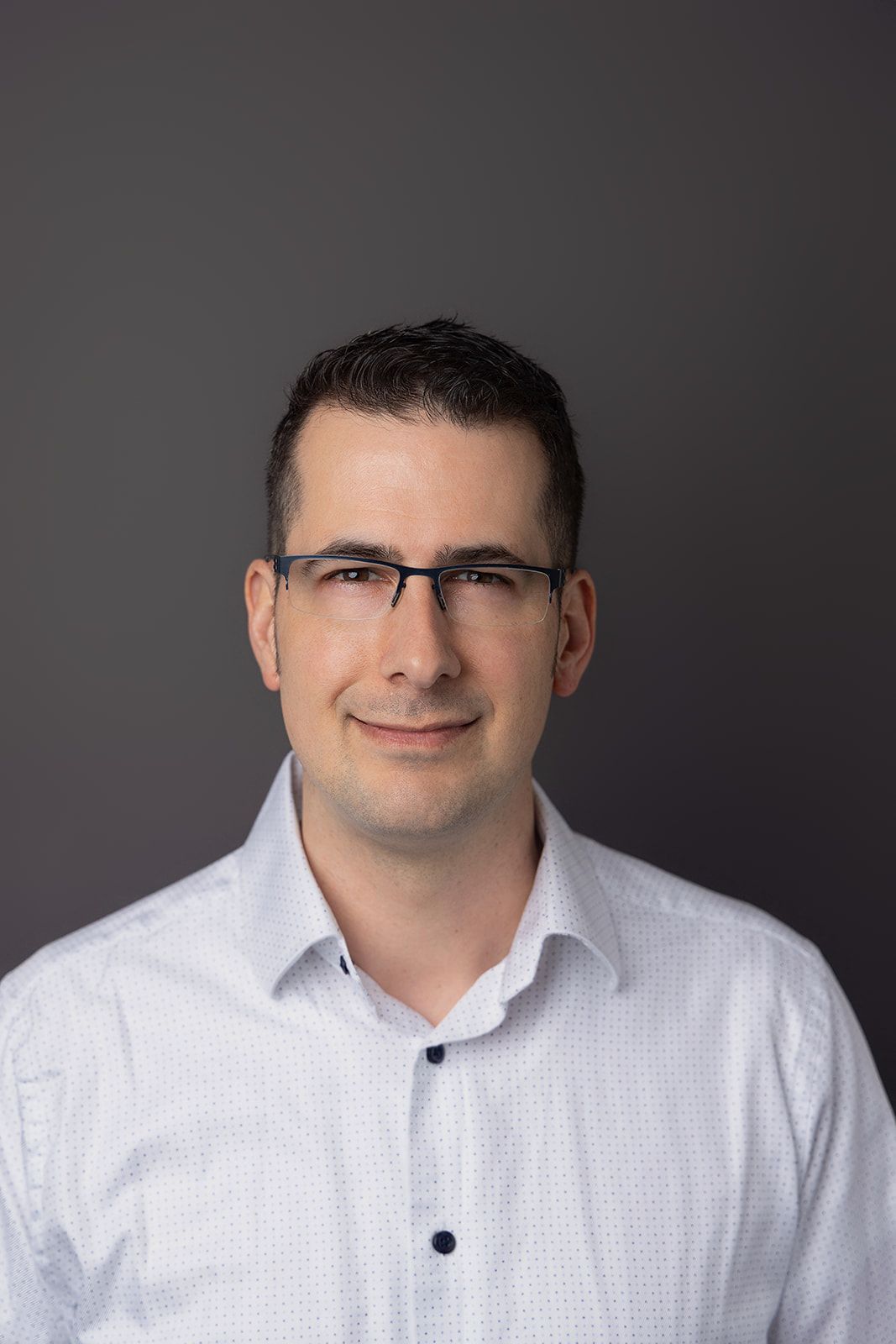 A man wearing glasses and a white shirt is smiling for the camera.