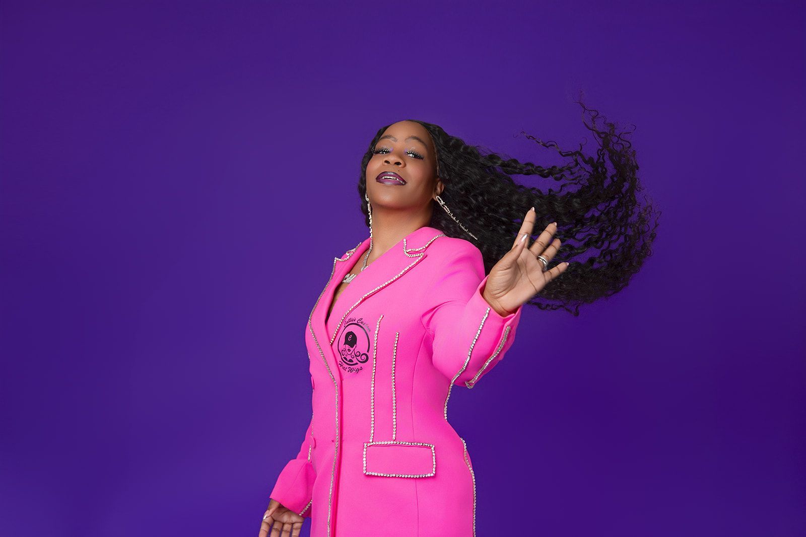 A woman in a pink suit is standing in front of a purple background.