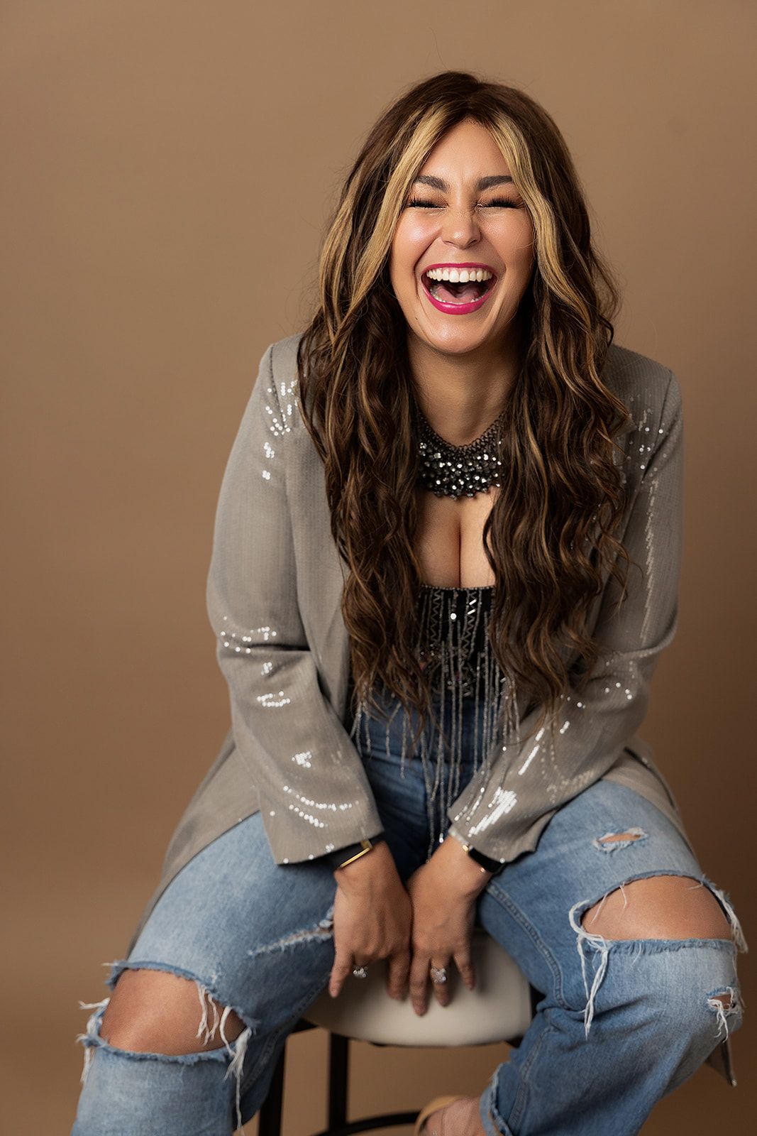 A woman is sitting on a stool with her mouth open and laughing.