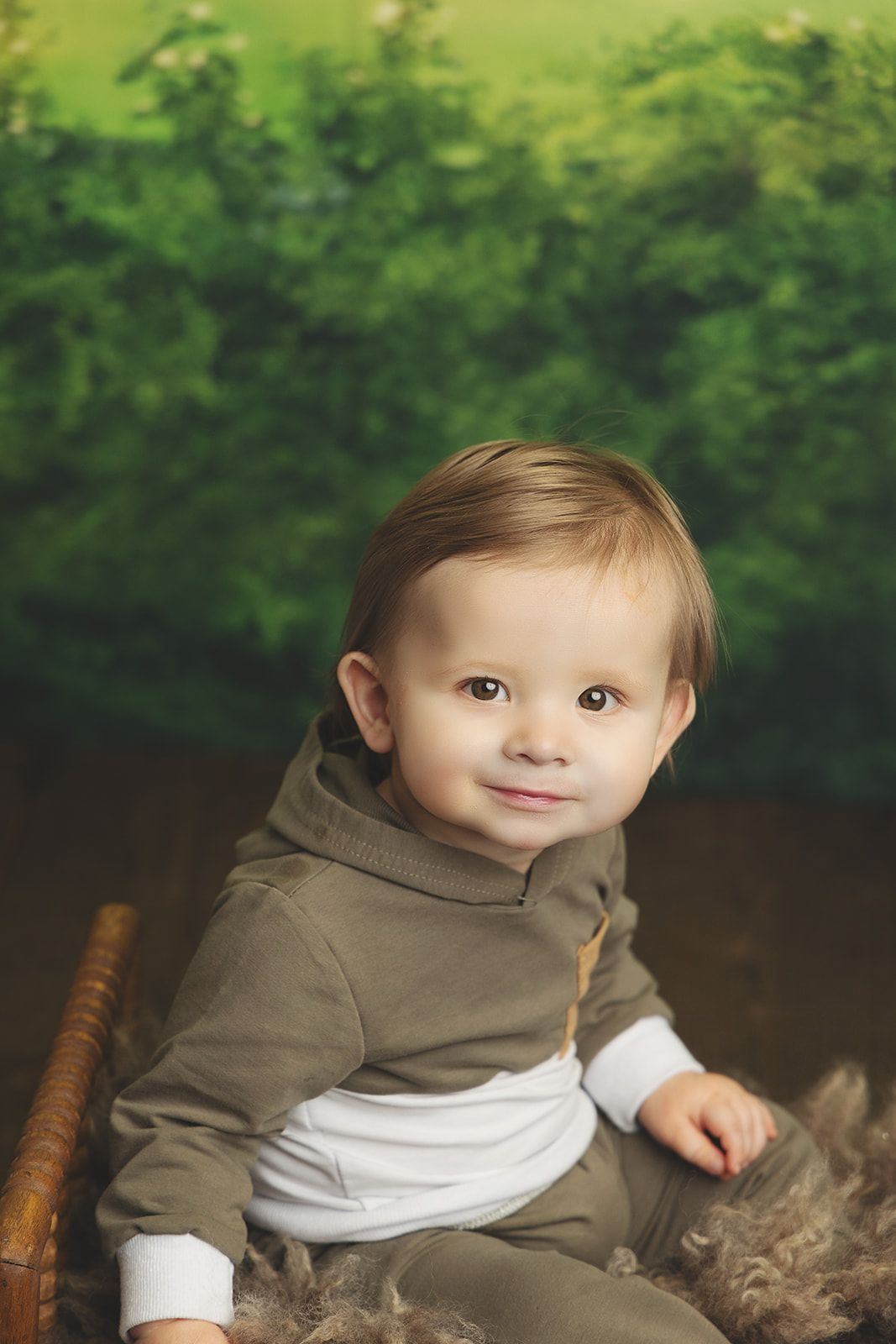 A baby boy is sitting in a basket in front of a green background