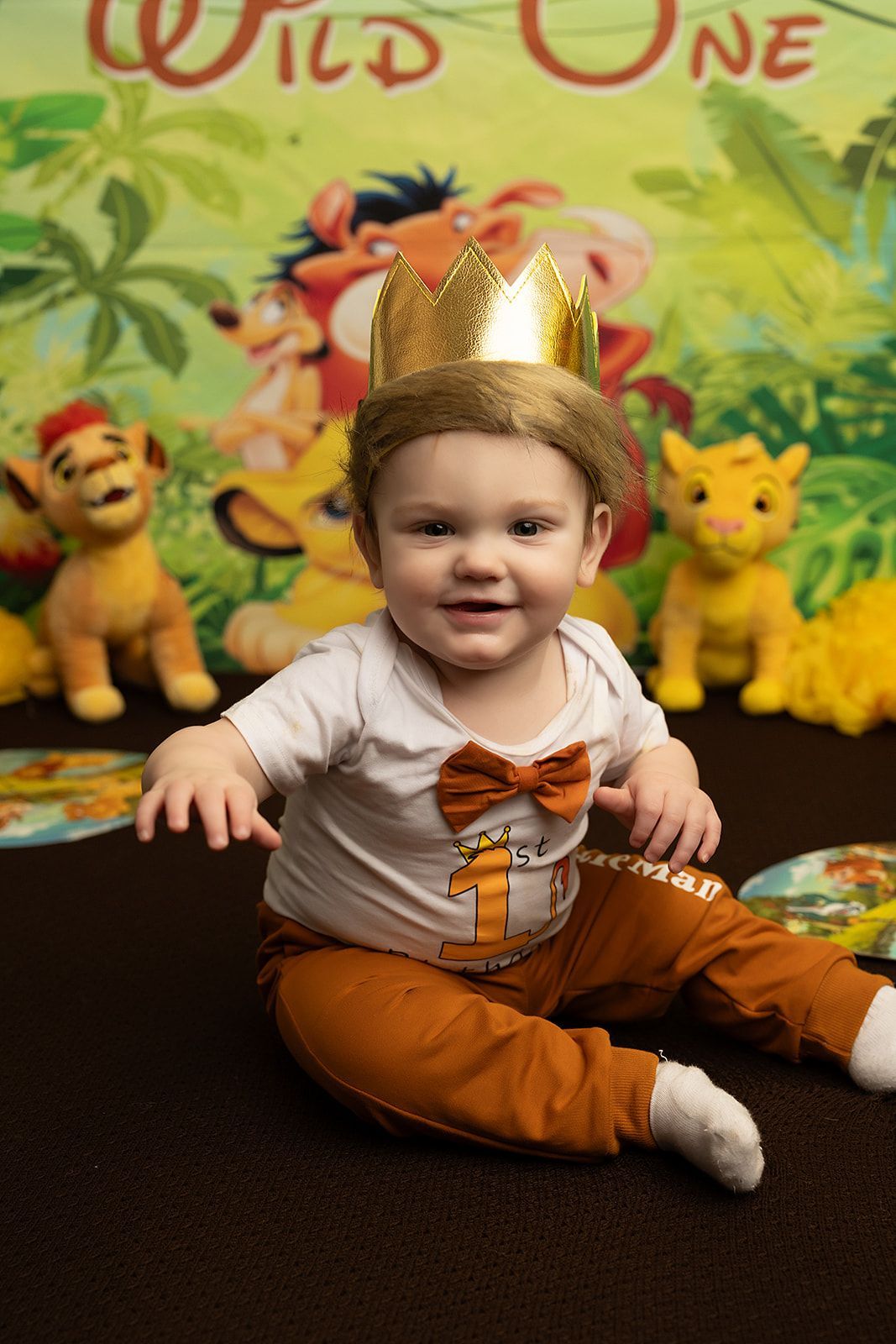 A baby is sitting on the floor wearing a crown and a bow tie