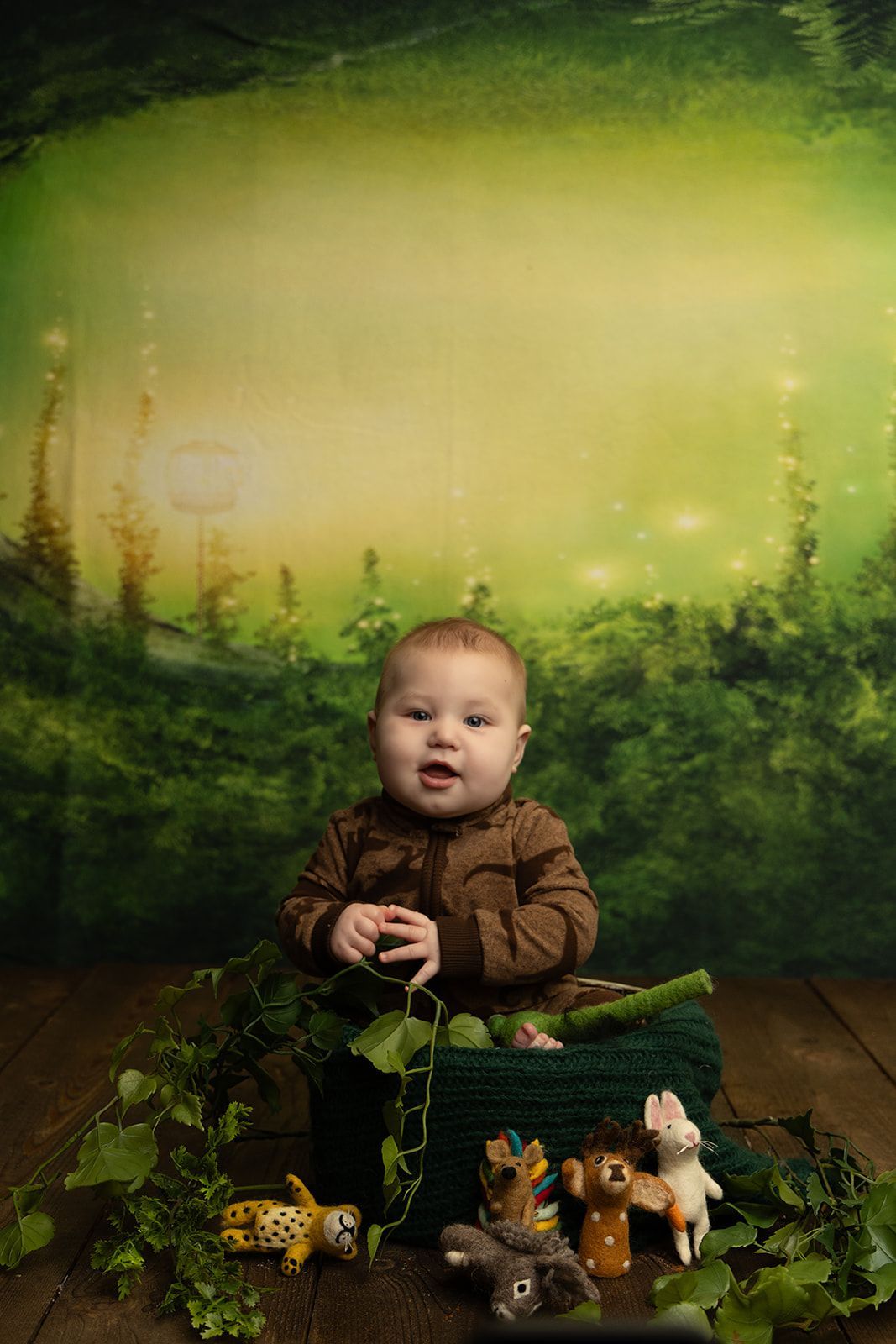 A baby is sitting in a basket with stuffed animals in front of a green background