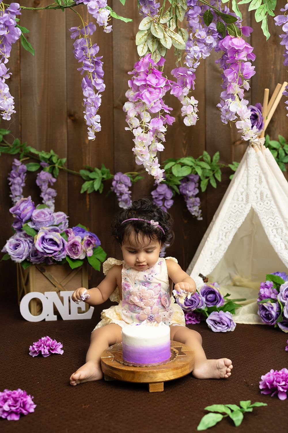 A baby girl is sitting on a wooden table with a cake