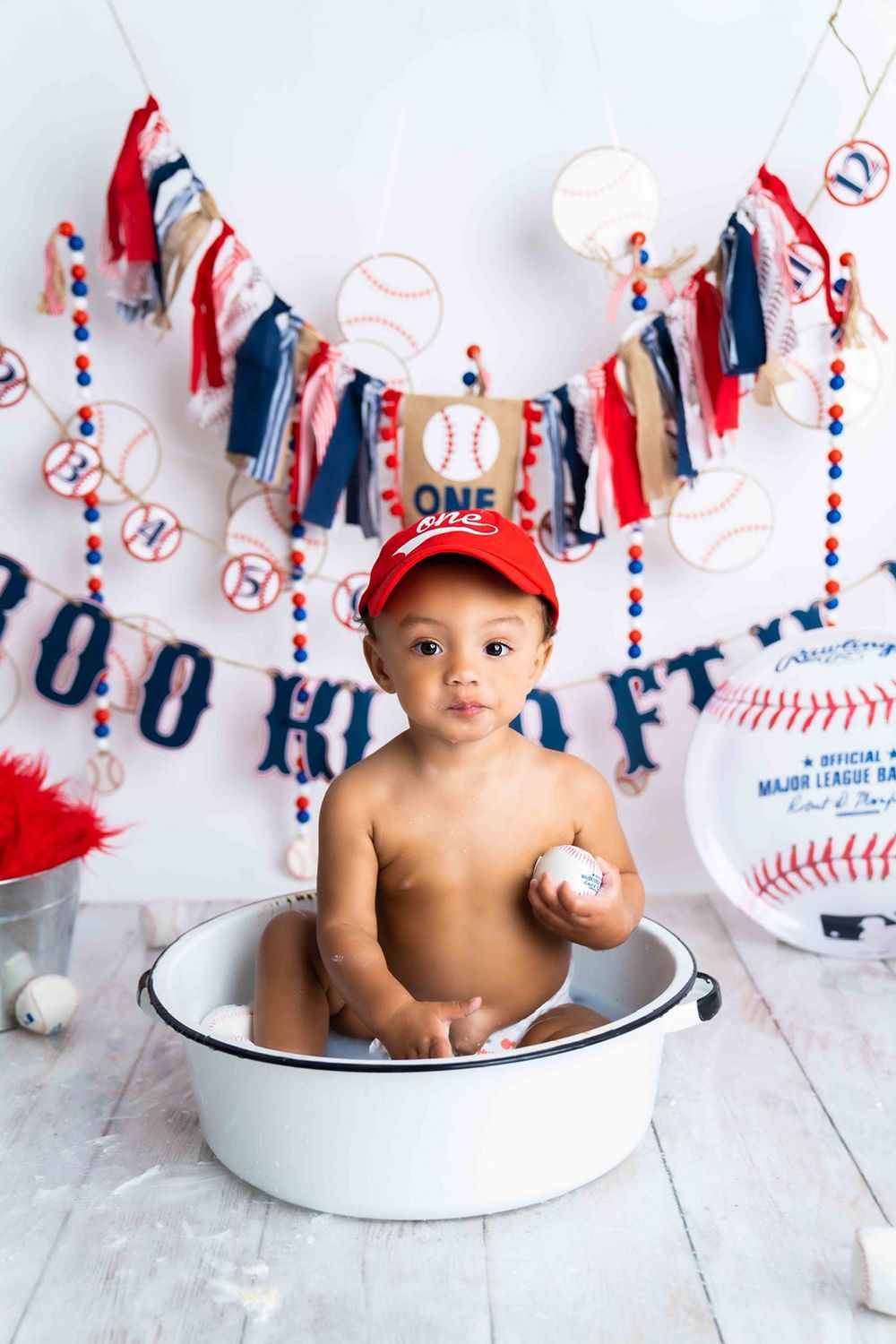 A baby is sitting in a bowl holding a baseball