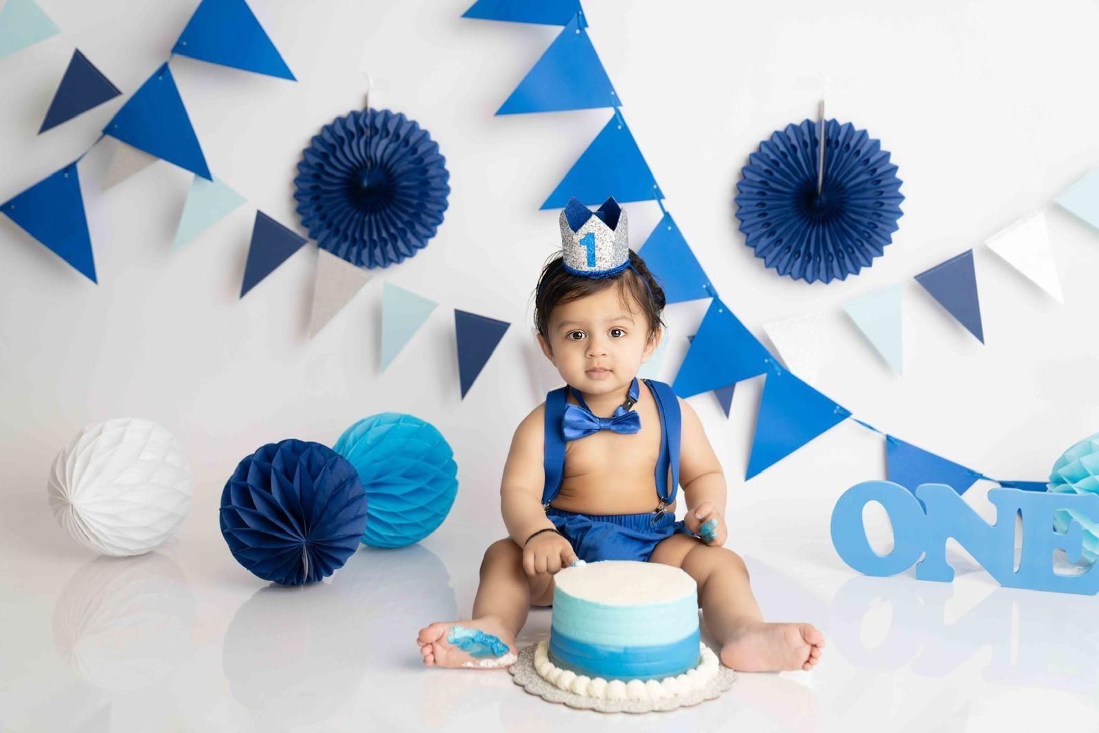 A baby is sitting on the floor with a cake and a crown on his head