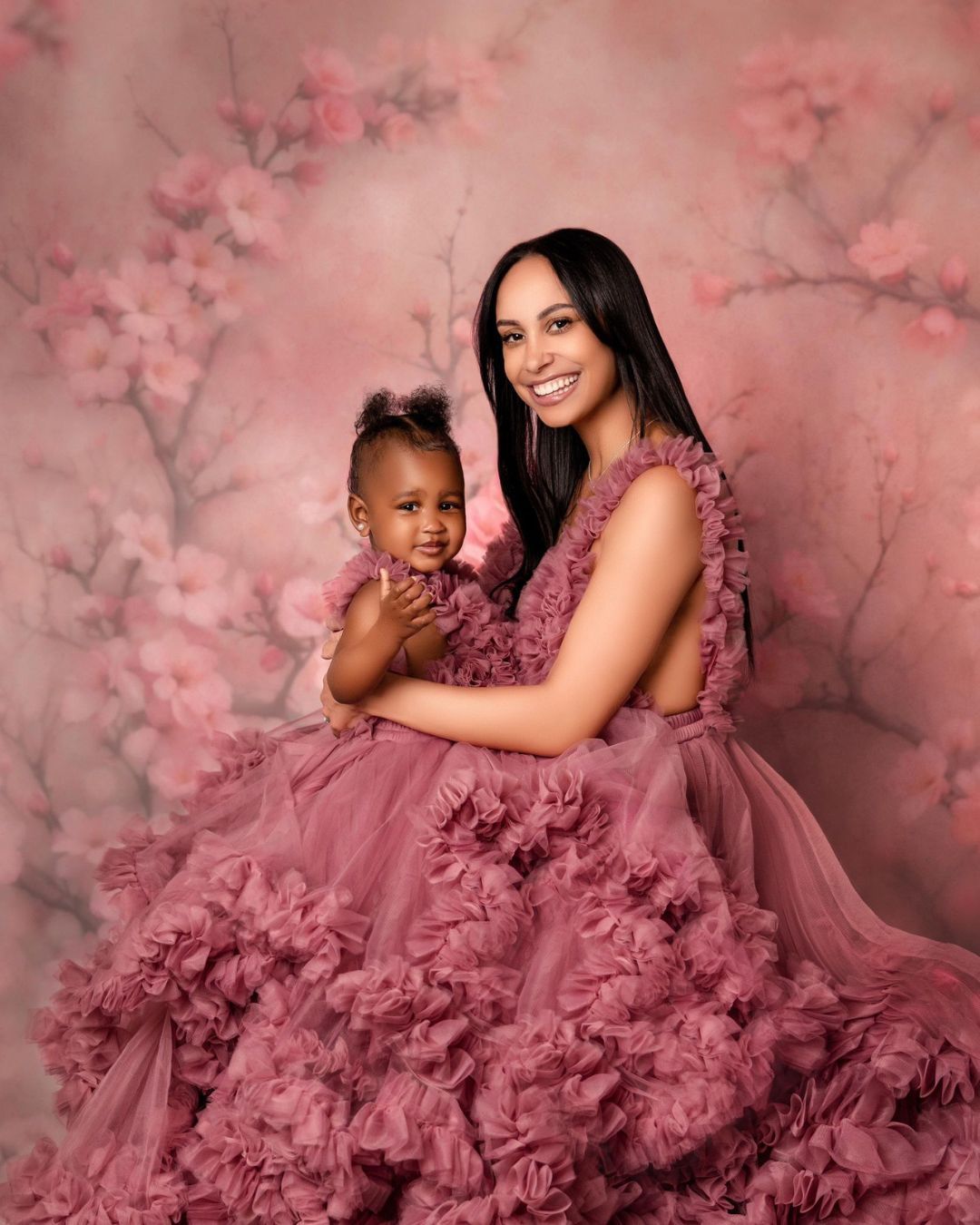 A woman in a pink dress is holding a baby in her arms.